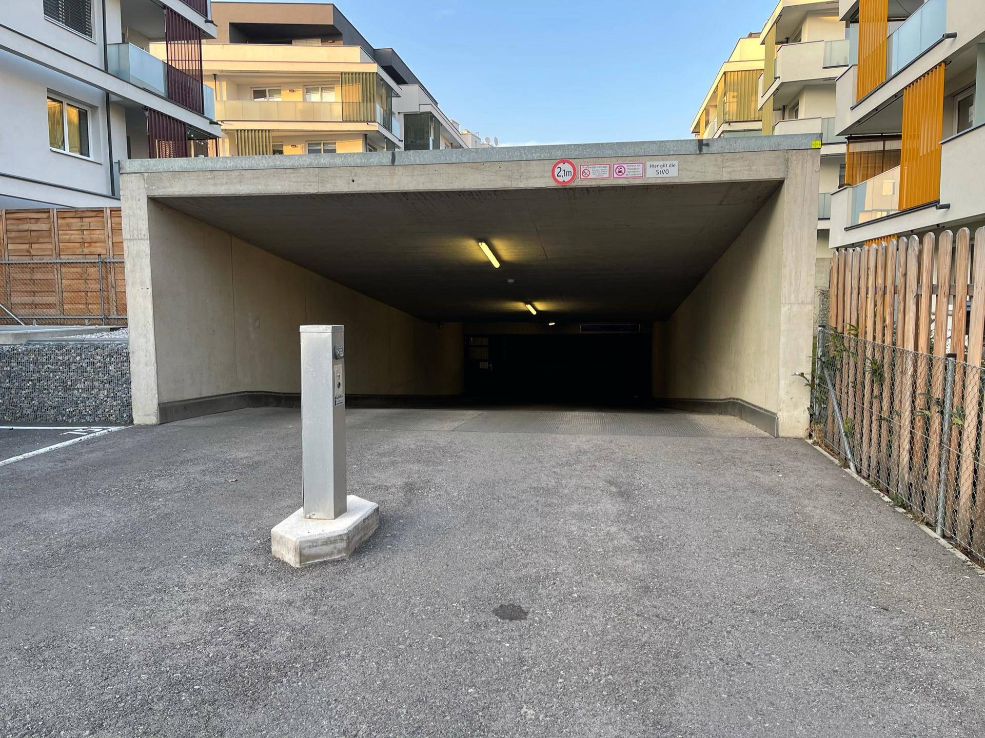 Eingangsbereich einer Tiefgarage mit modernen Wohngebäuden im Hintergrund und Zugangskontrolle.
