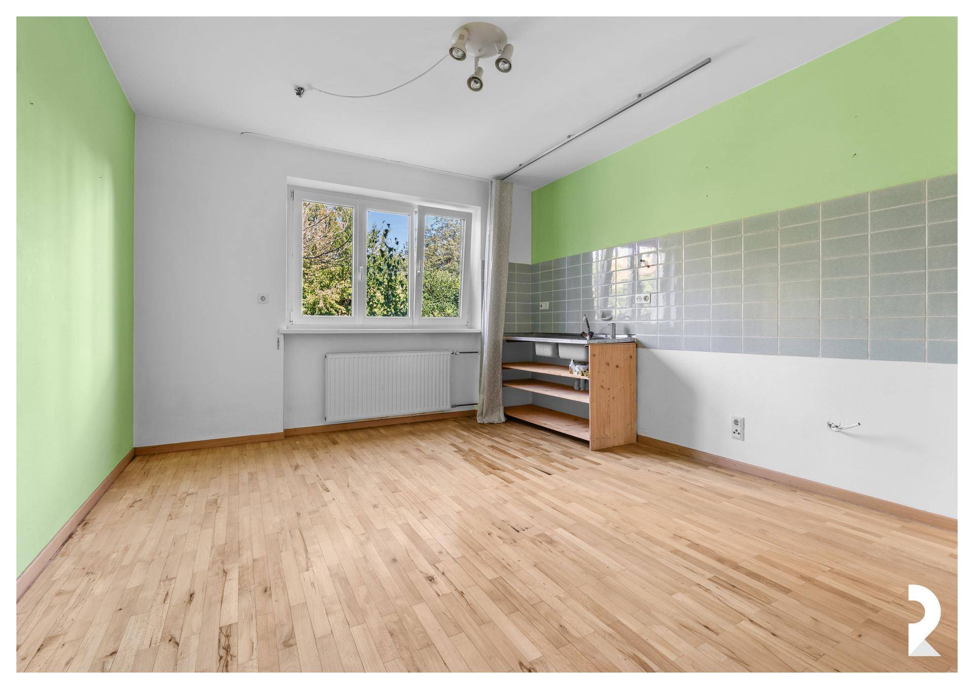 Einfache Küche mit grünen Wänden, Holzboden und Fenster mit Blick ins Grüne.