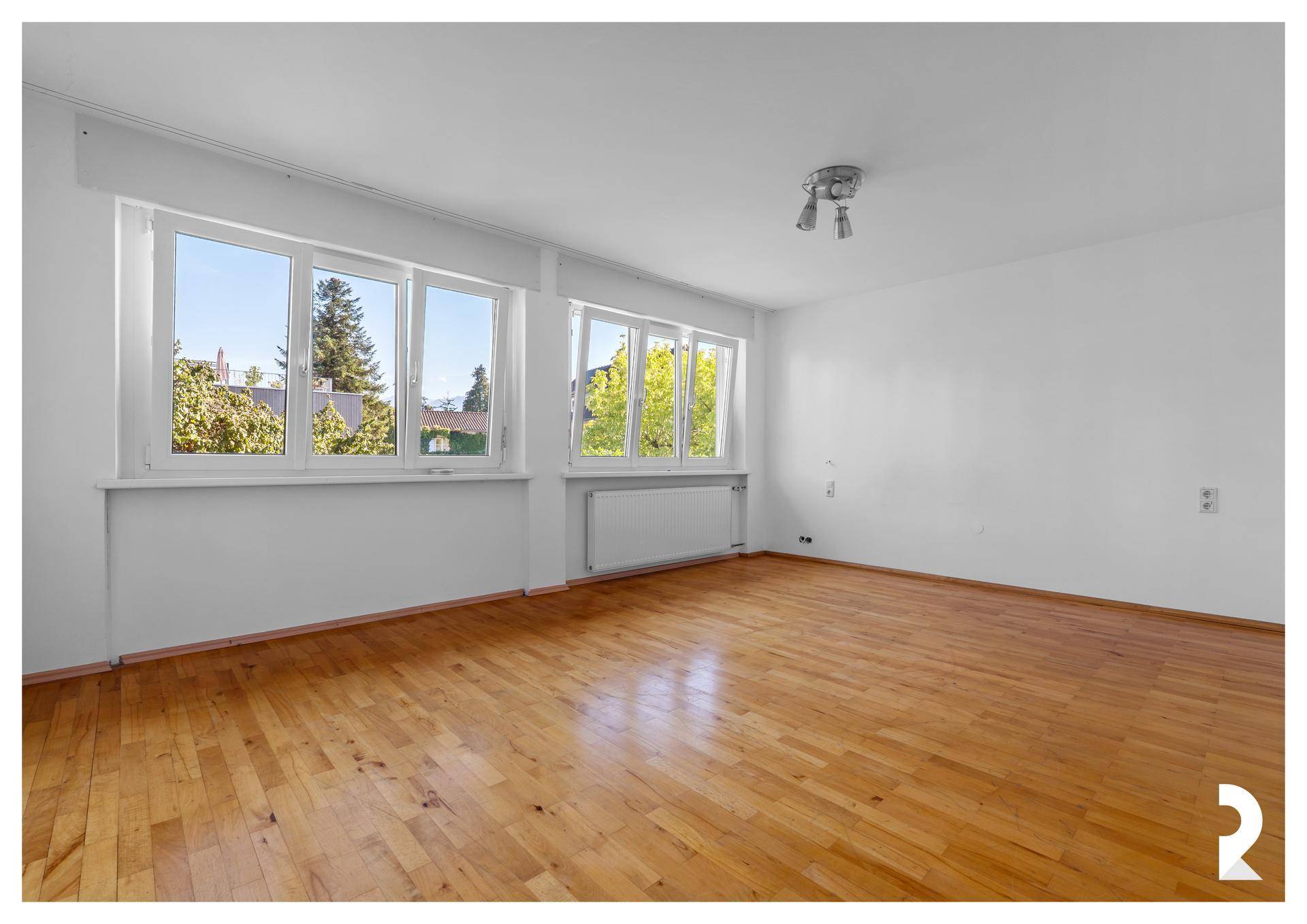 Helles Schlafzimmer mit Holzboden, weißen Wänden und großen Fenstern mit Blick ins Grüne.