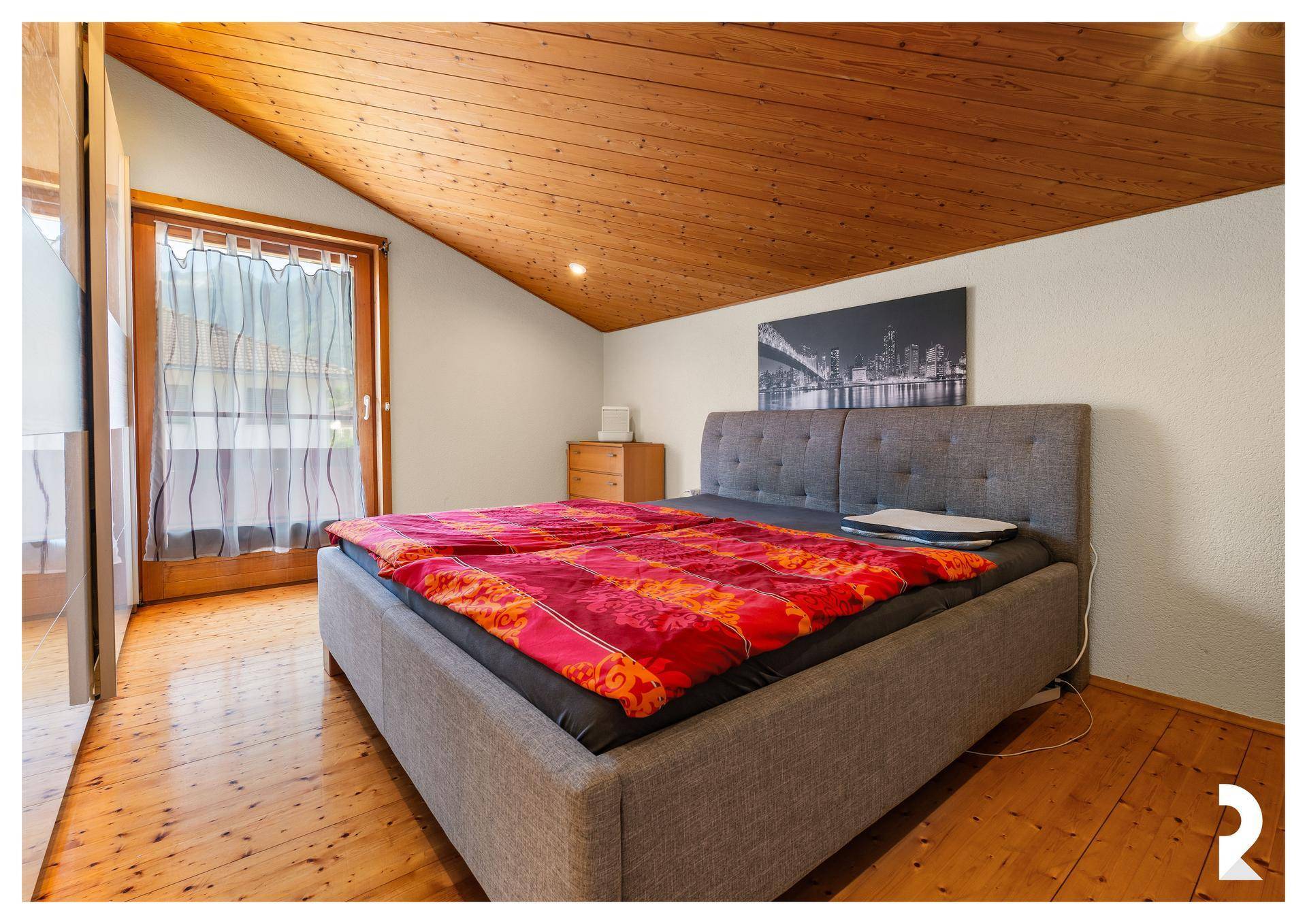 Gemütliches Schlafzimmer mit Holzbalkendecke, Holzboden und Zugang zum Balkon.