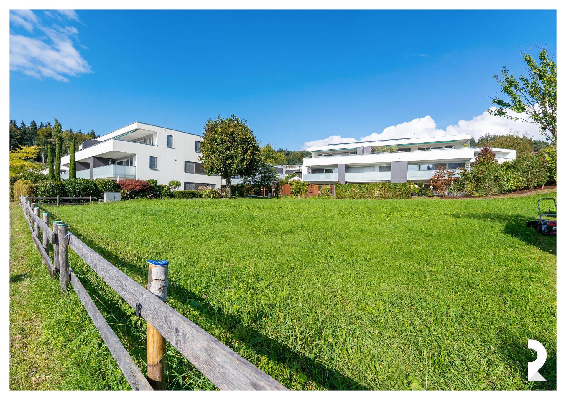 Baugrundstück mit Holzzaun im Vordergrund und modernen Wohngebäuden in der Ferne.