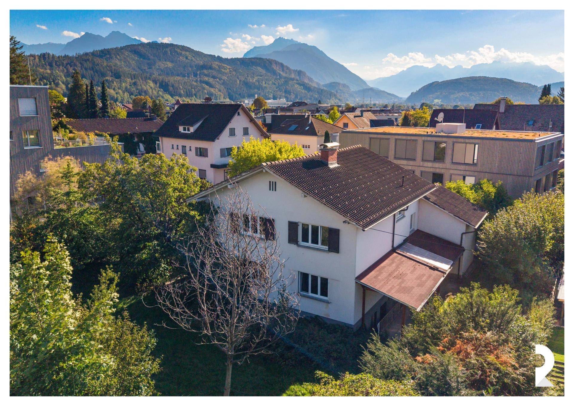 Luftaufnahme des Hauses mit umliegender Bebauung und einer beeindruckenden Bergkulisse im Hintergrund.