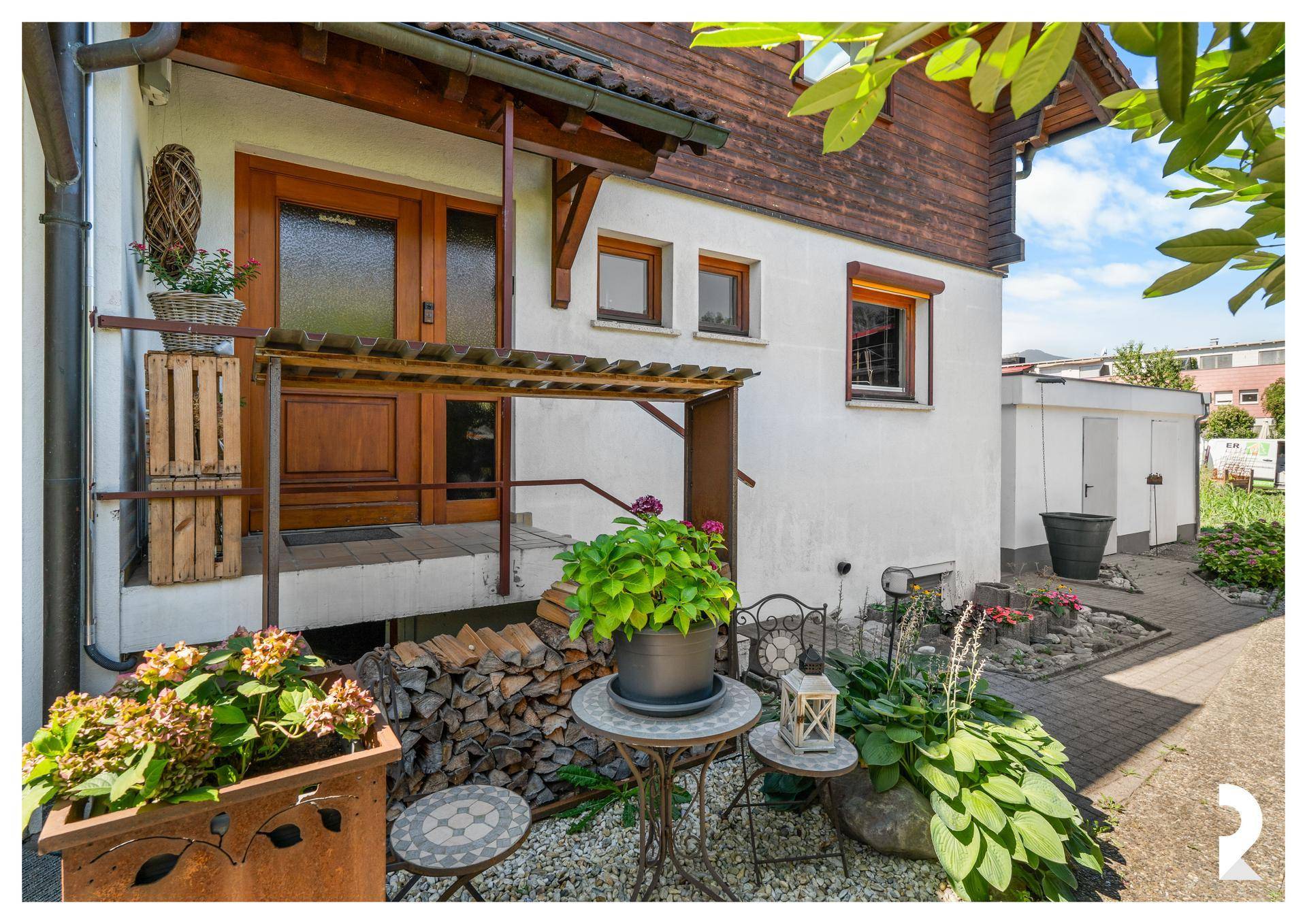 Eingangsbereich des Hauses mit Holzverkleidung, kleiner Sitzecke und dekorativen Pflanzen.