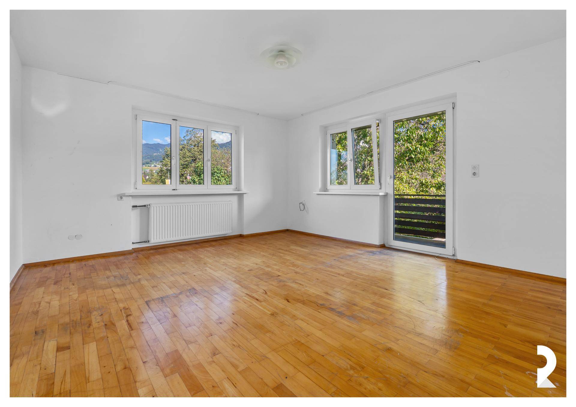 Schlafzimmer mit Holzboden, weißen Wänden und Zugang zu einem Balkon.