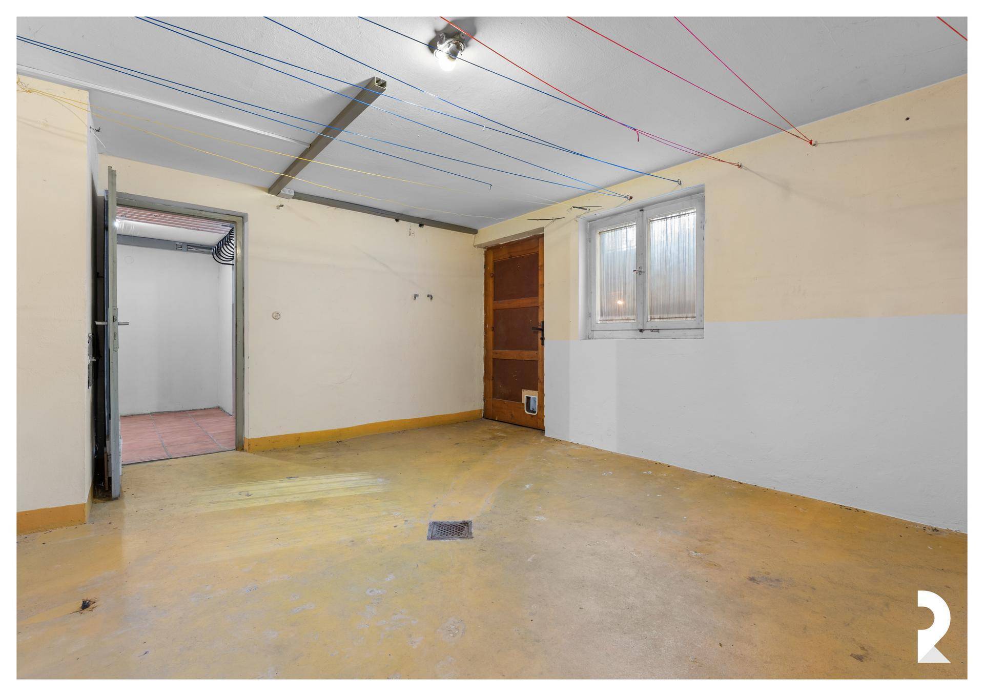 Kellerraum mit gelbem Boden, Fenster und Wäscheleinen an der Decke.