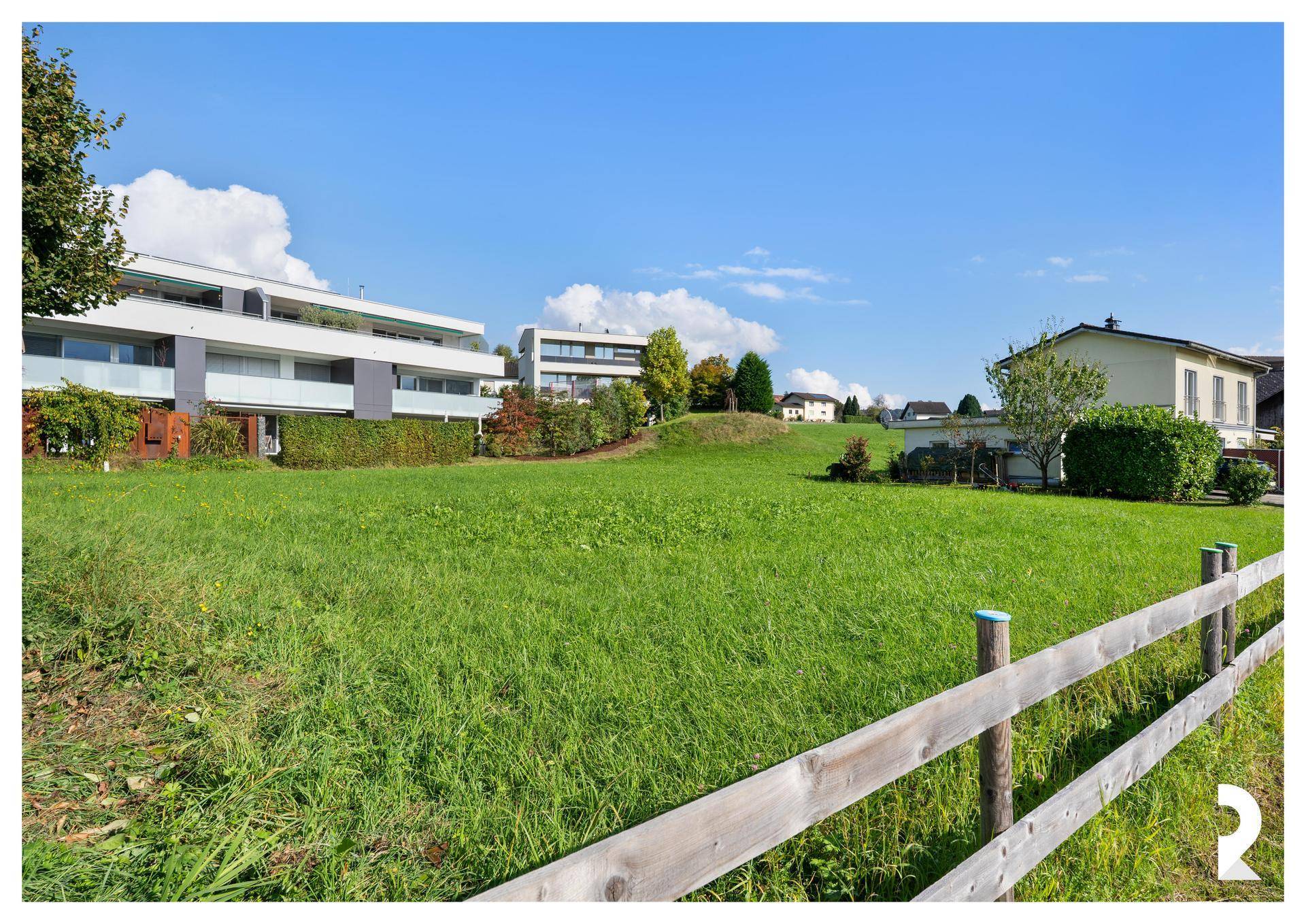 Weitläufiges Baugrundstück mit Holzzaun und Blick auf die umliegende Wohnbebauung.