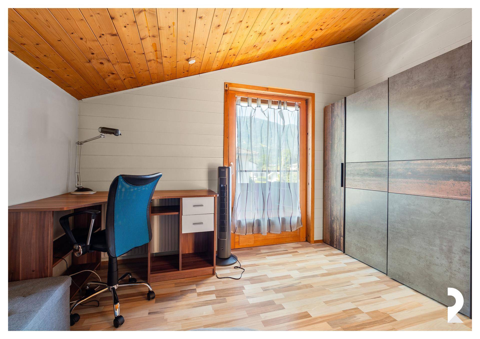 Helles Arbeitszimmer mit Schreibtisch, Kleiderschrank und Zugang zum Balkon.