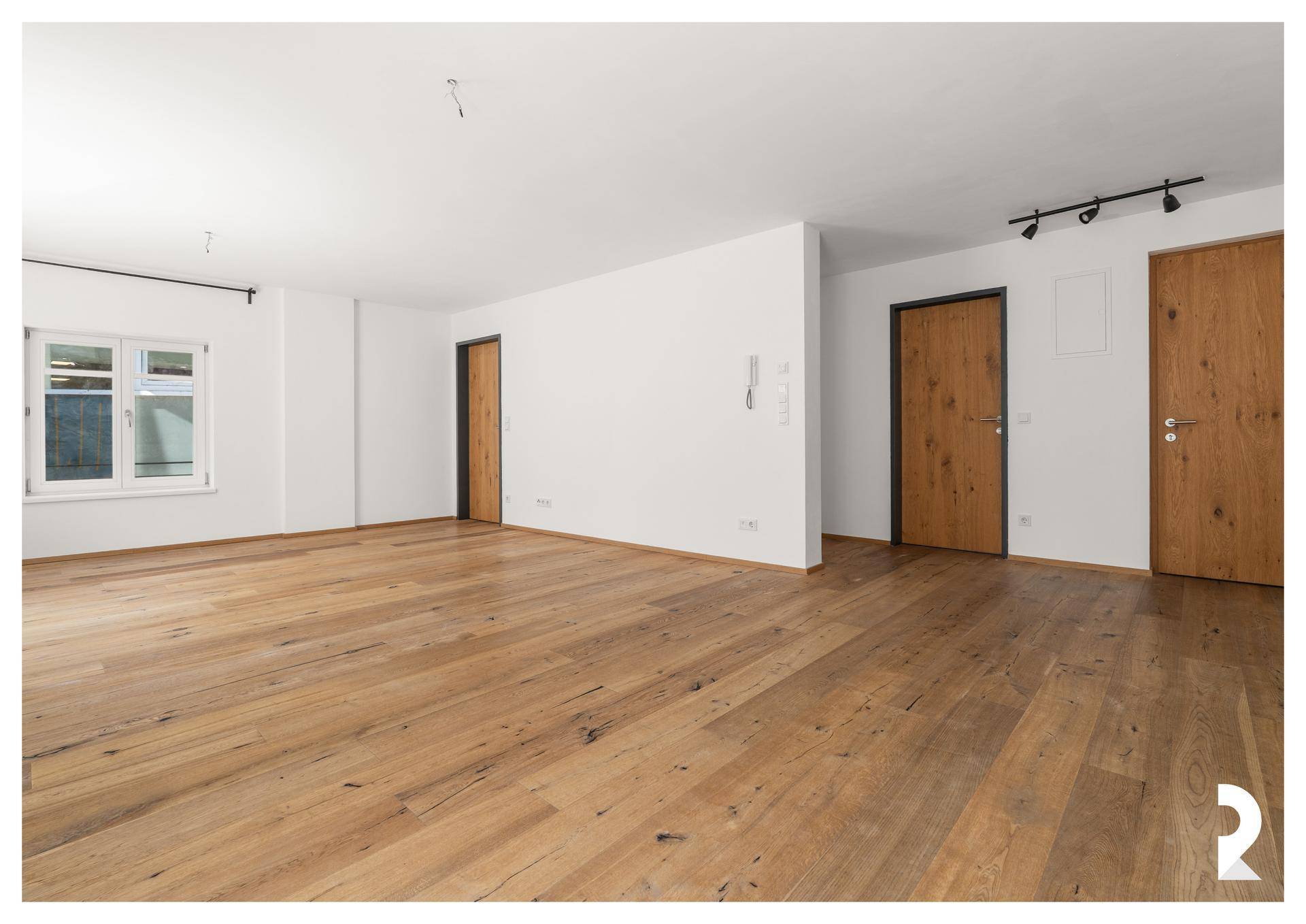 Heller Raum mit Holzboden, weißen Wänden und zwei Holztüren, der vielseitig genutzt werden kann.
