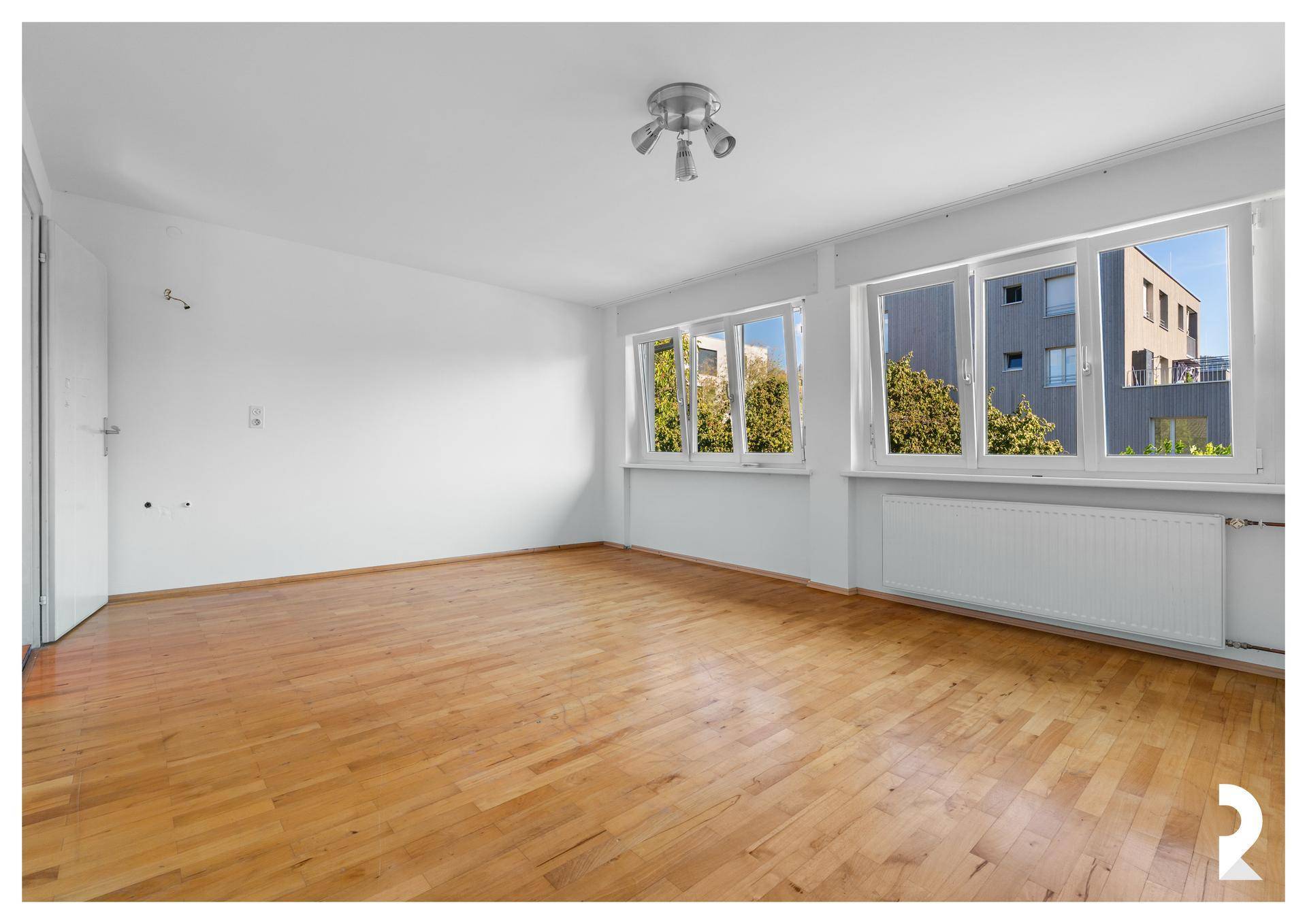 Schlafzimmer mit Holzboden, weißen Wänden und Blick auf die umliegenden Gebäude.