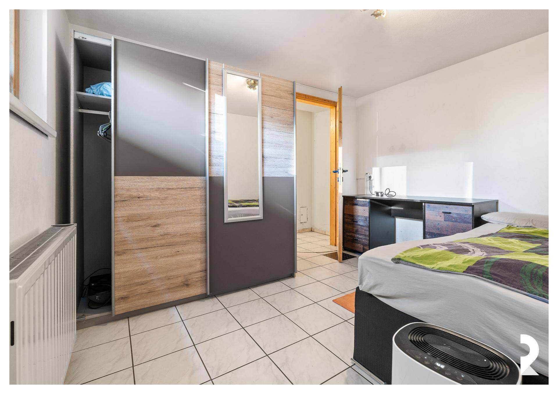 Helles Schlafzimmer mit Fliesenboden, großem Kleiderschrank und Schreibtisch.