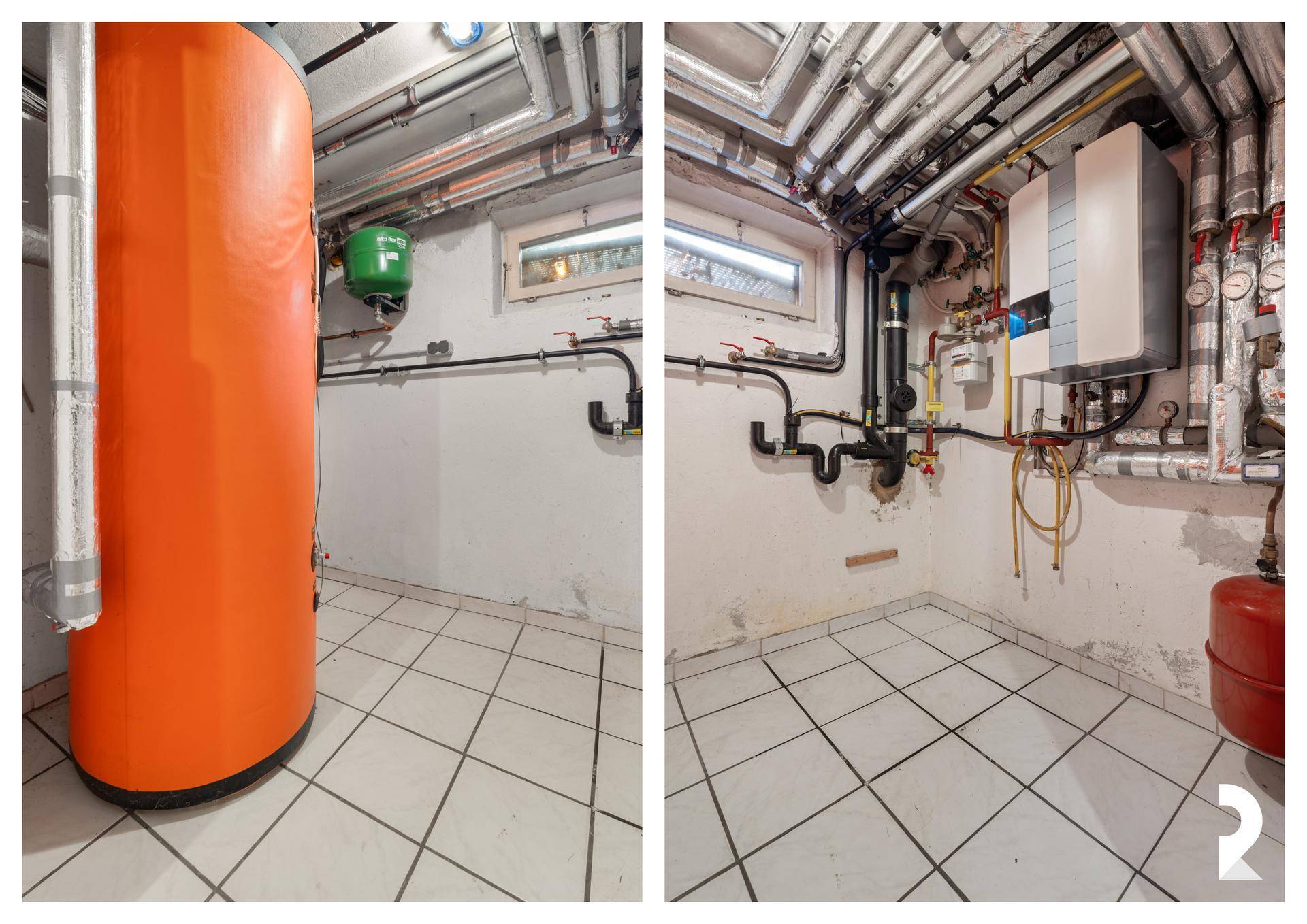 Heizungsraum im Keller mit Warmwasserspeicher und zahlreichen Rohren.