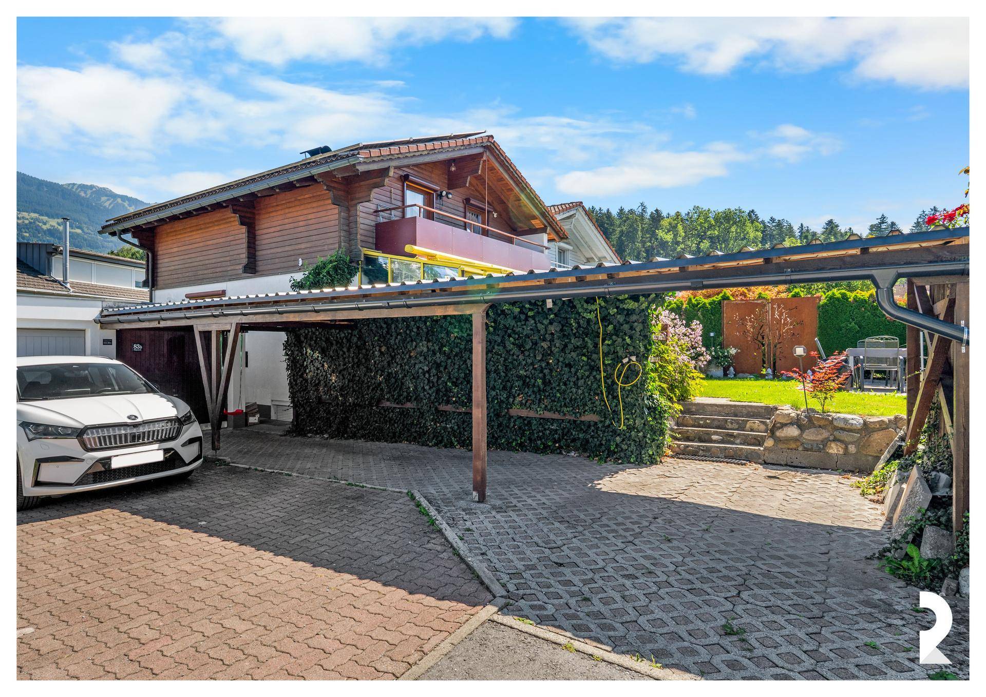 Überdachter Carport und gepflasterte Einfahrt neben dem Haus mit Zugang zum Garten.