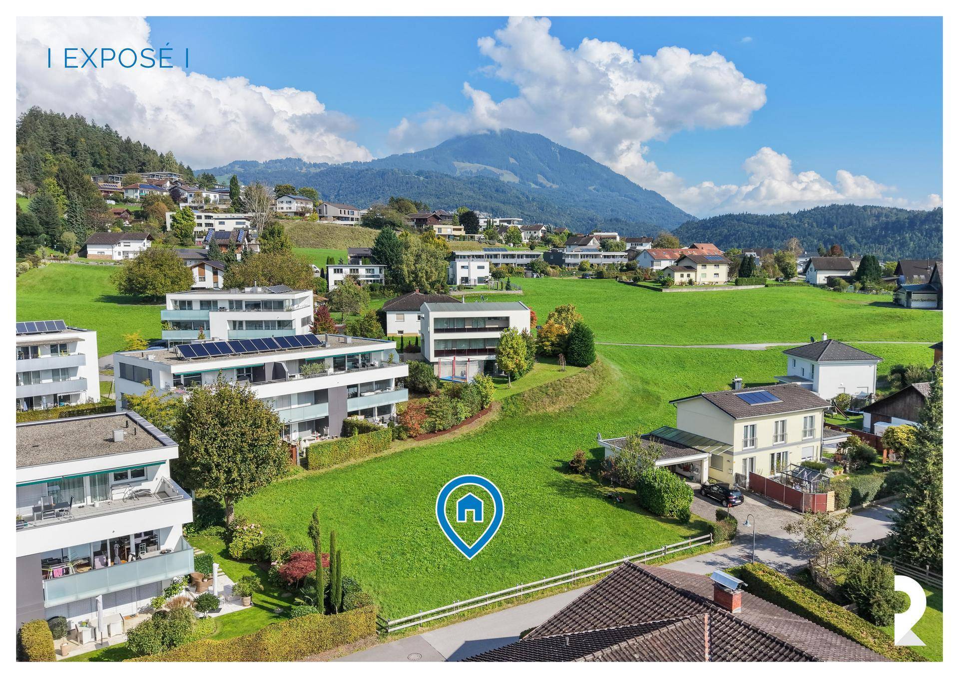 Luftaufnahme des Baugrundstücks in einer grünen Umgebung mit Bergblick und umliegenden Häusern.