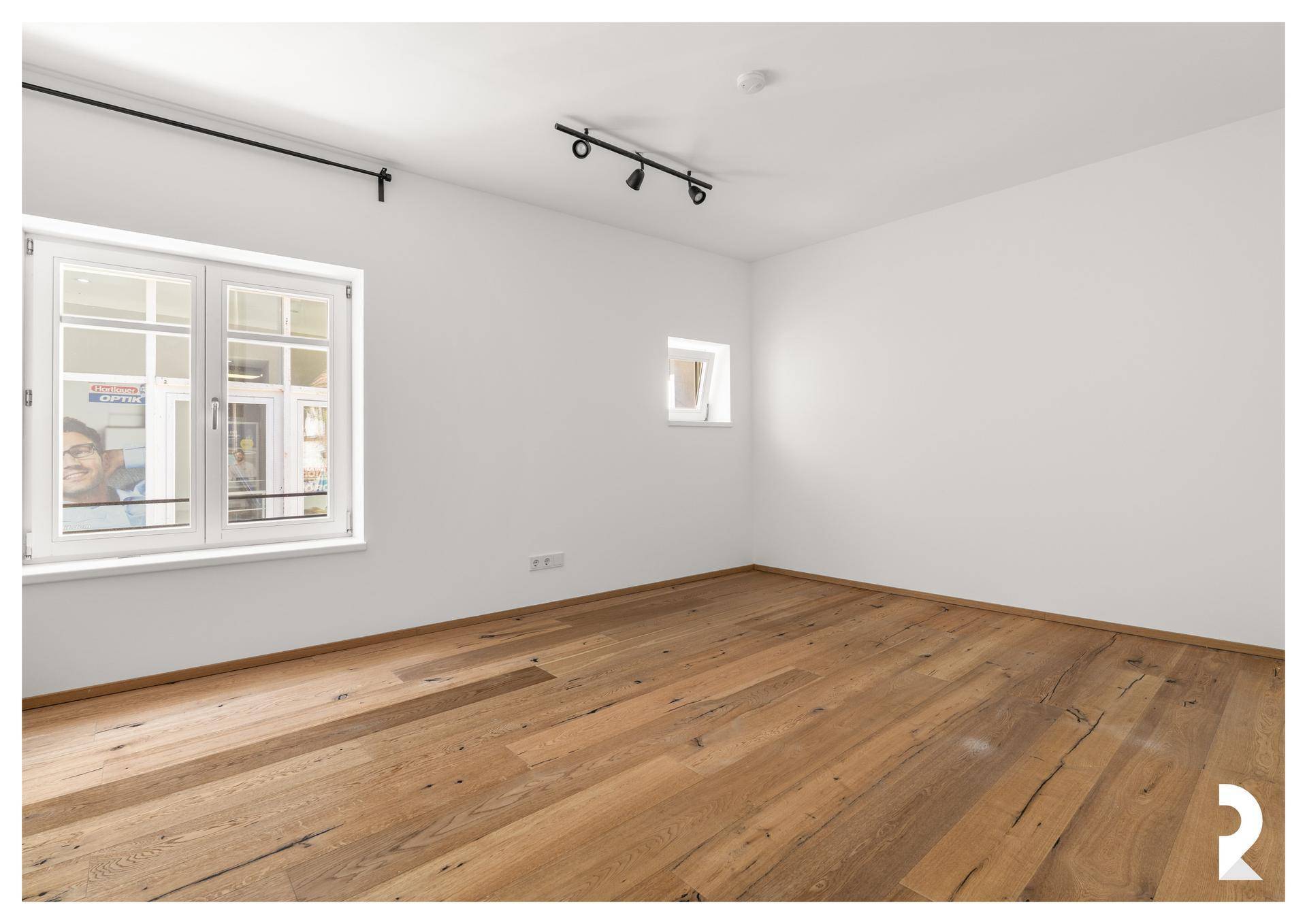 Heller Raum mit Holzboden und zwei Fenstern, der vielseitig als Schlaf- oder Arbeitszimmer genutzt werden kann.