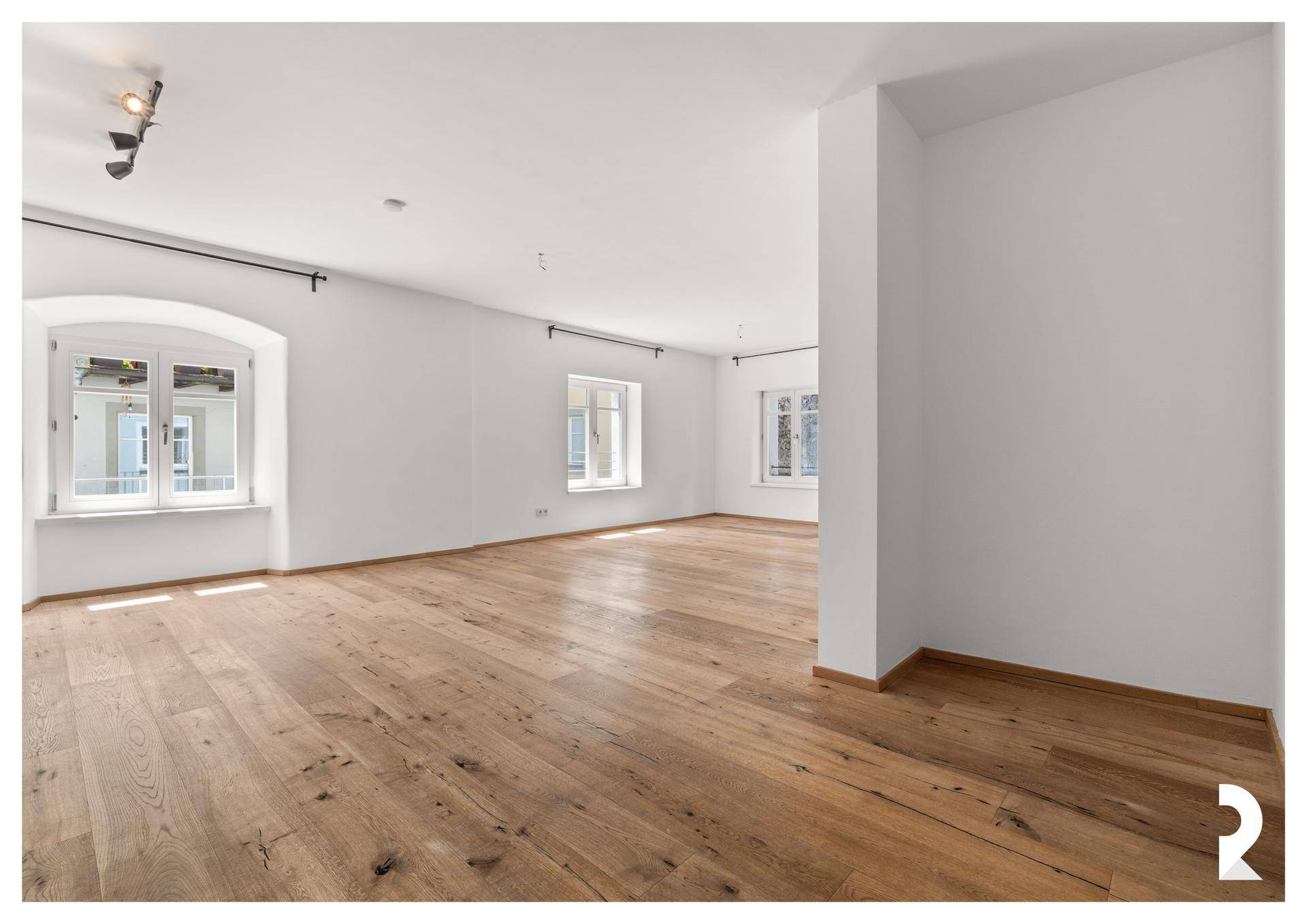 Geräumiger, heller Raum mit Holzboden, weißen Wänden und mehreren Fenstern, bereit zur individuellen Gestaltung.