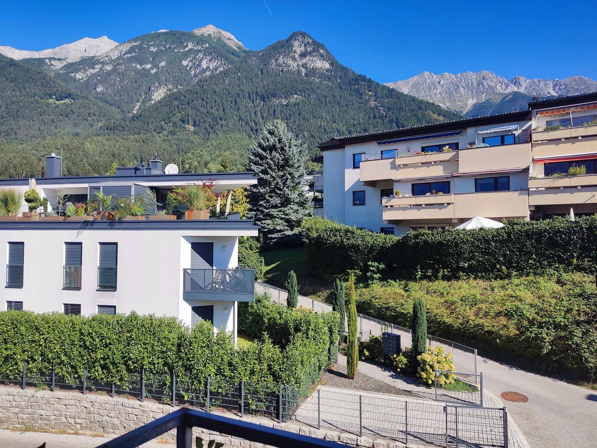 Panoramablick auf die umliegende Berglandschaft und moderne Wohngebäude in sonniger Lage.
