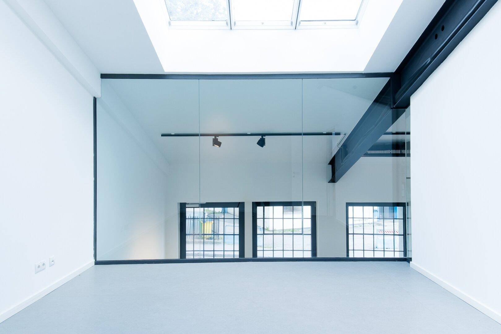 Heller Flur im Obergeschoss mit Glasgeländer und Blick auf die unteren Räume durch große Fenster.