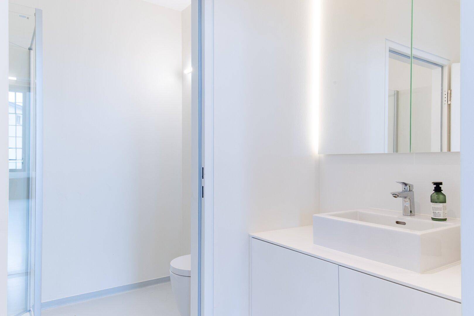 Modernes Badezimmer mit weißem Waschtisch, integriertem Spiegel und minimalistischem Design.