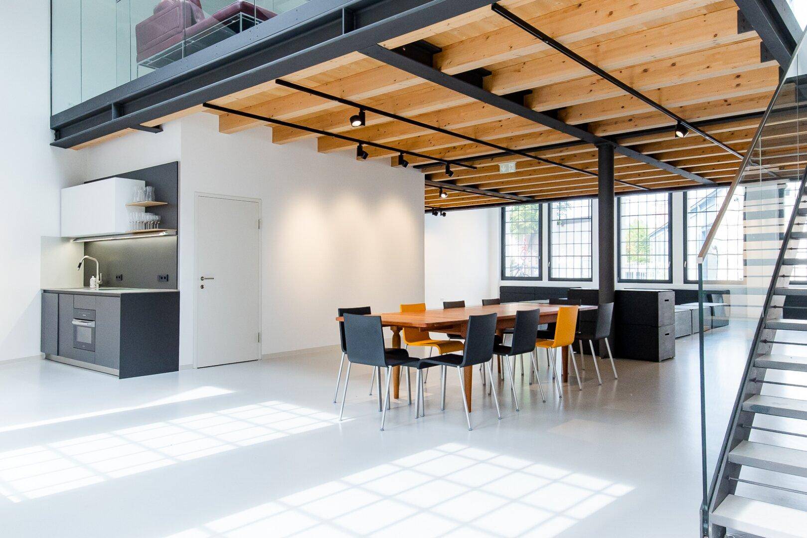 Moderner Essbereich in einem offenen Loft mit Holzbalkendecke und großen Fenstern.