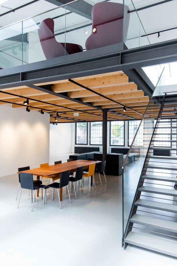 Essbereich mit Holztisch und Stühlen unter einer Galerie in einem hellen Loftraum.