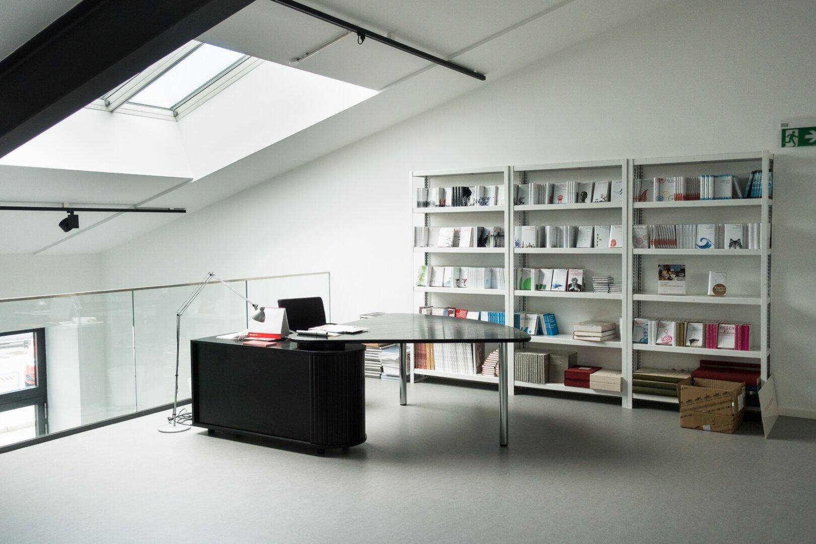 Arbeitsbereich auf einer Galerie mit Dachfenster, Bücherregalen und modernem Schreibtisch.