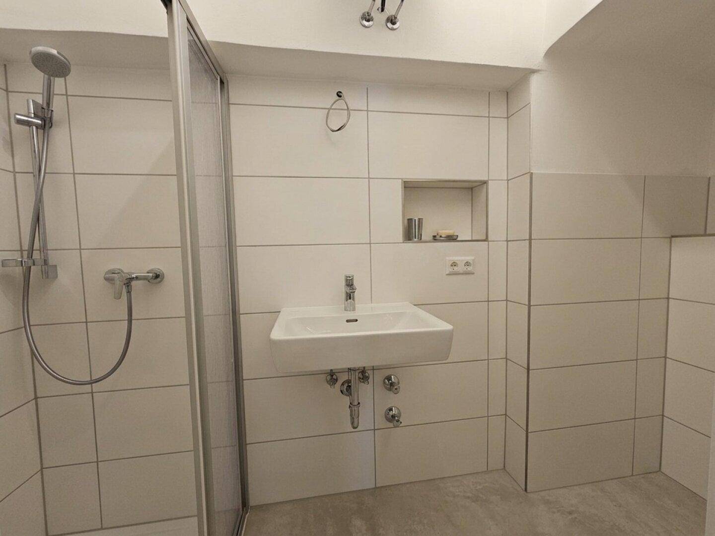 Helles Badezimmer mit Duschkabine, modernem Waschbecken und weißen Wandfliesen.