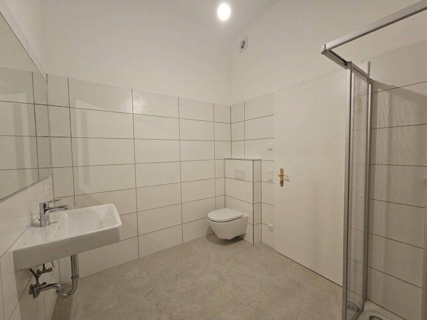 Modernes Badezimmer mit weißen Fliesen, wandhängendem WC und Duschkabine.