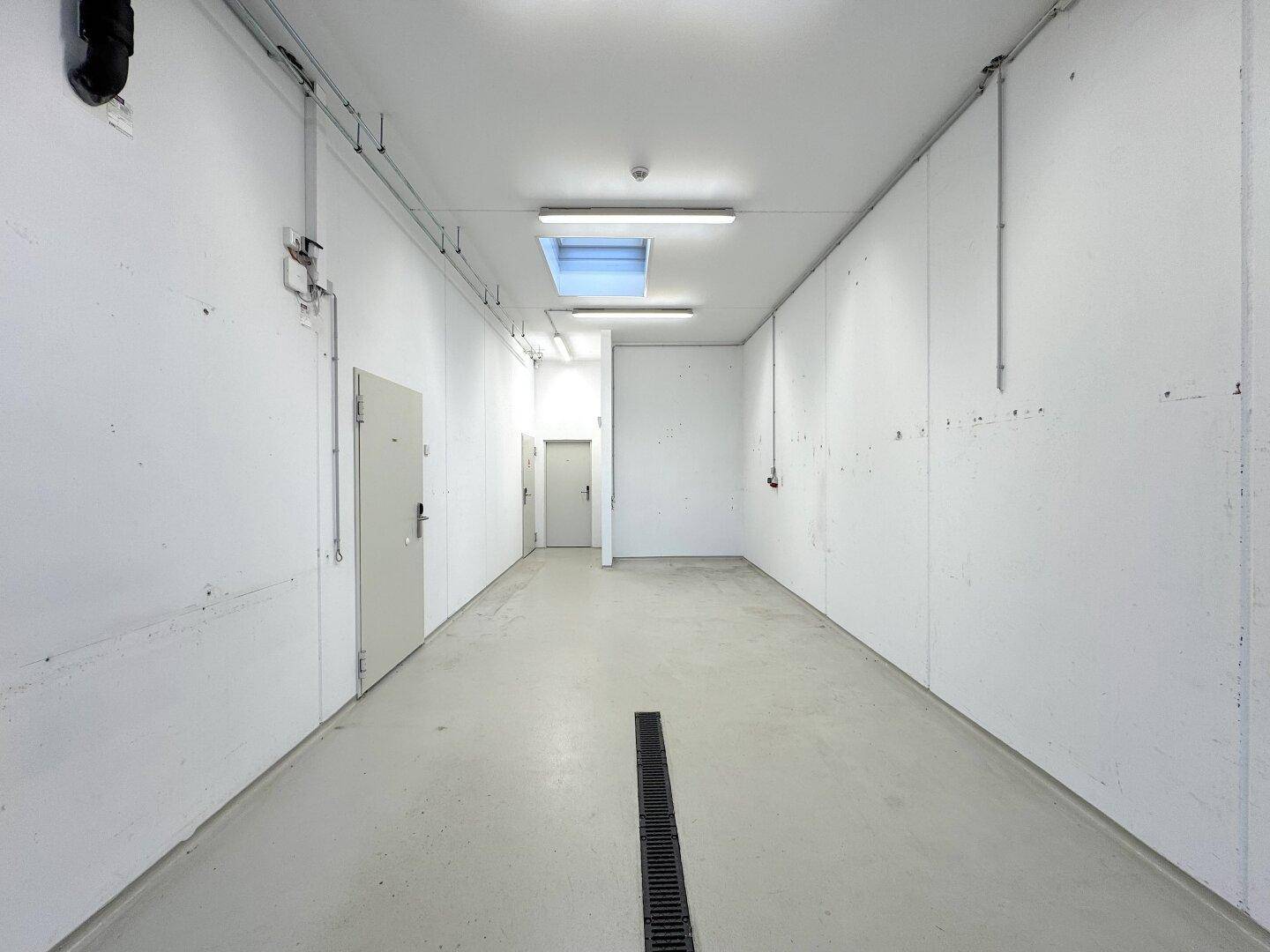 Langer, sauberer Garagenraum mit Oberlicht, weißen Wänden und Zugang zu weiteren Räumen.