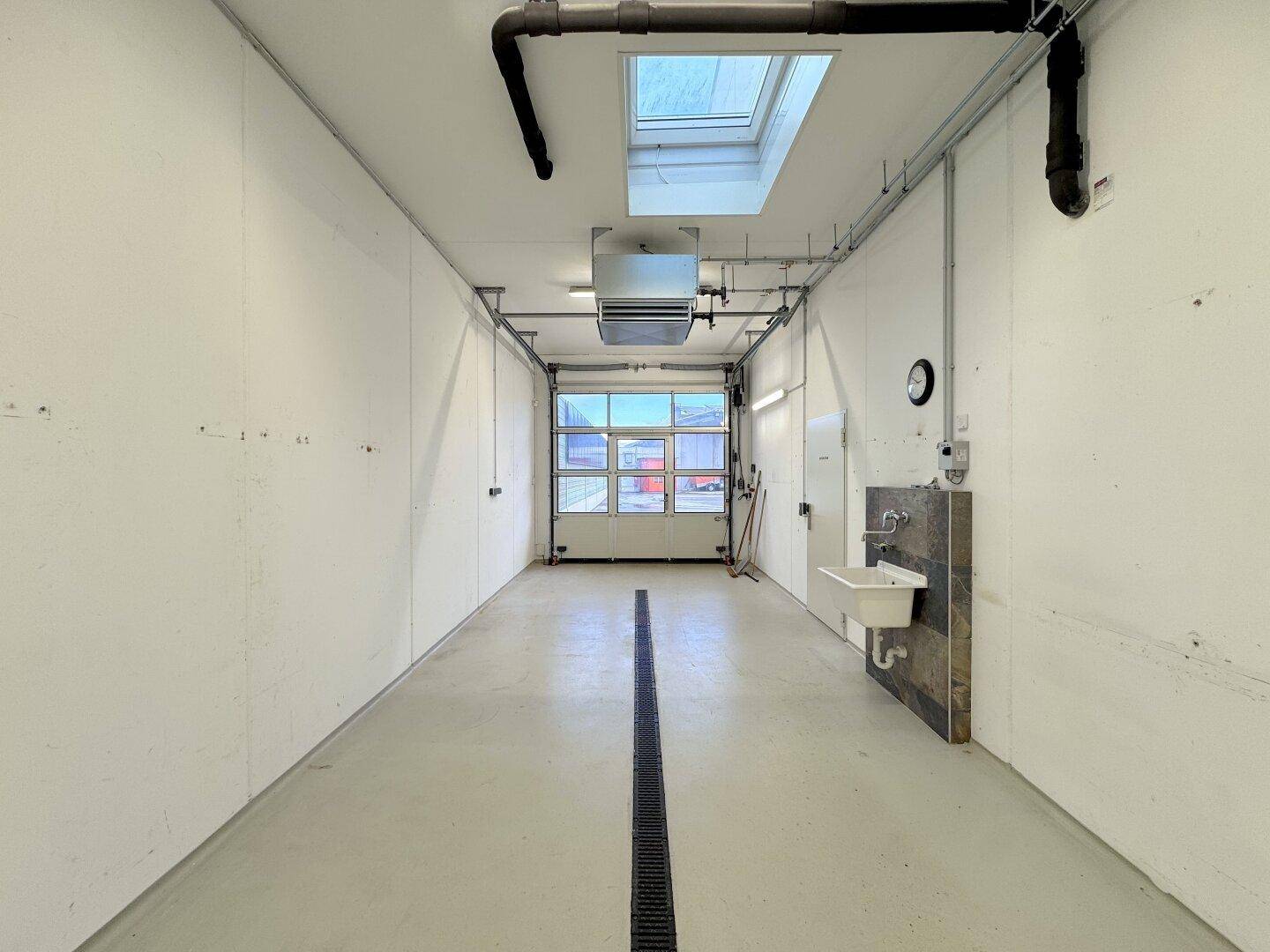 Geräumige Garage mit Rolltor, Oberlicht und Waschbecken, ideal für Fahrzeuge oder Lagerung.
