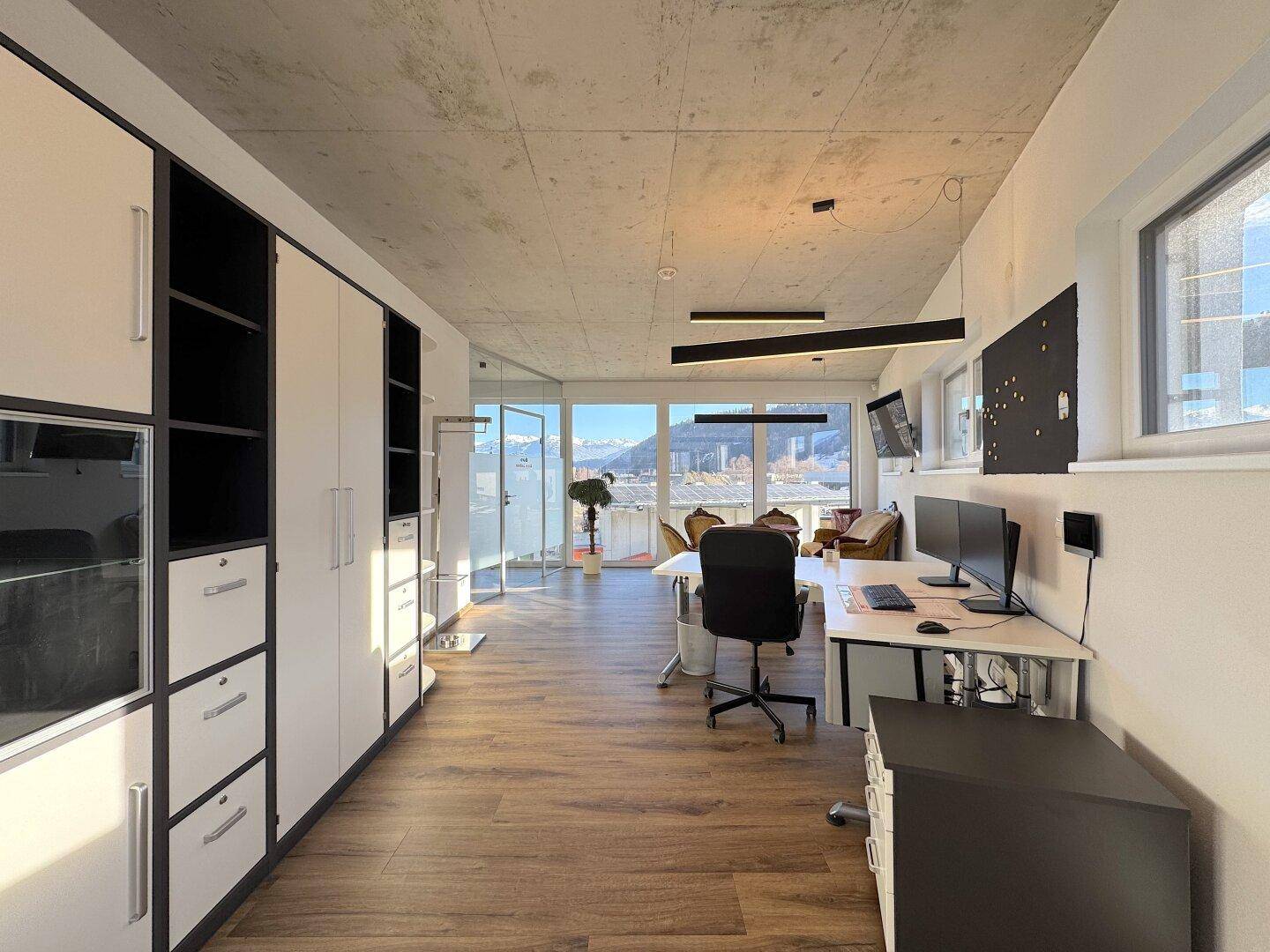 Modernes Büro mit Einbauschränken, Schreibtischen und Blick auf die umliegende Landschaft und Berge.