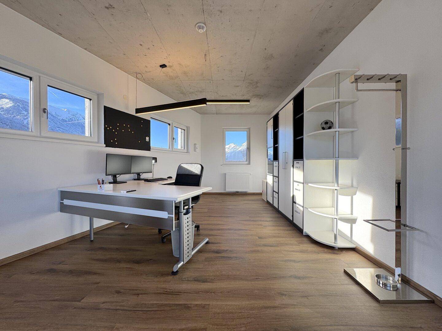 Helles Büro mit Schreibtisch, Regalen und Fenstern, die einen weiten Blick auf die Berglandschaft bieten.