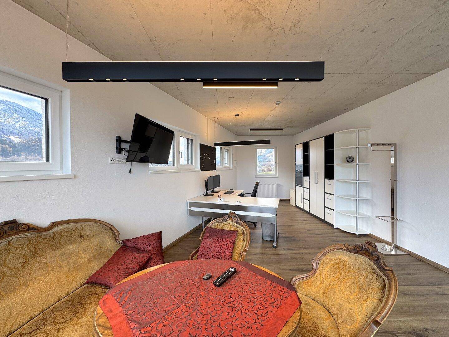 Geräumiges Büro mit Holzboden, modernen Leuchten und einer gemütlichen Sitzecke mit Bergblick.