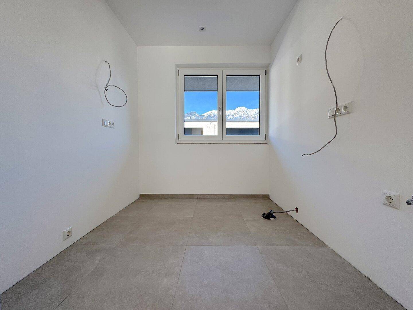 Kleiner, unmöblierter Raum mit Fliesenboden und einem Fenster mit Bergblick, ideal als Abstellraum.