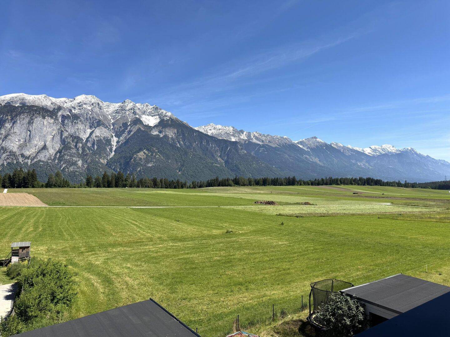 Weitläufiger Panoramablick auf die majestätischen Berge und die grünen Felder unter blauem Himmel.