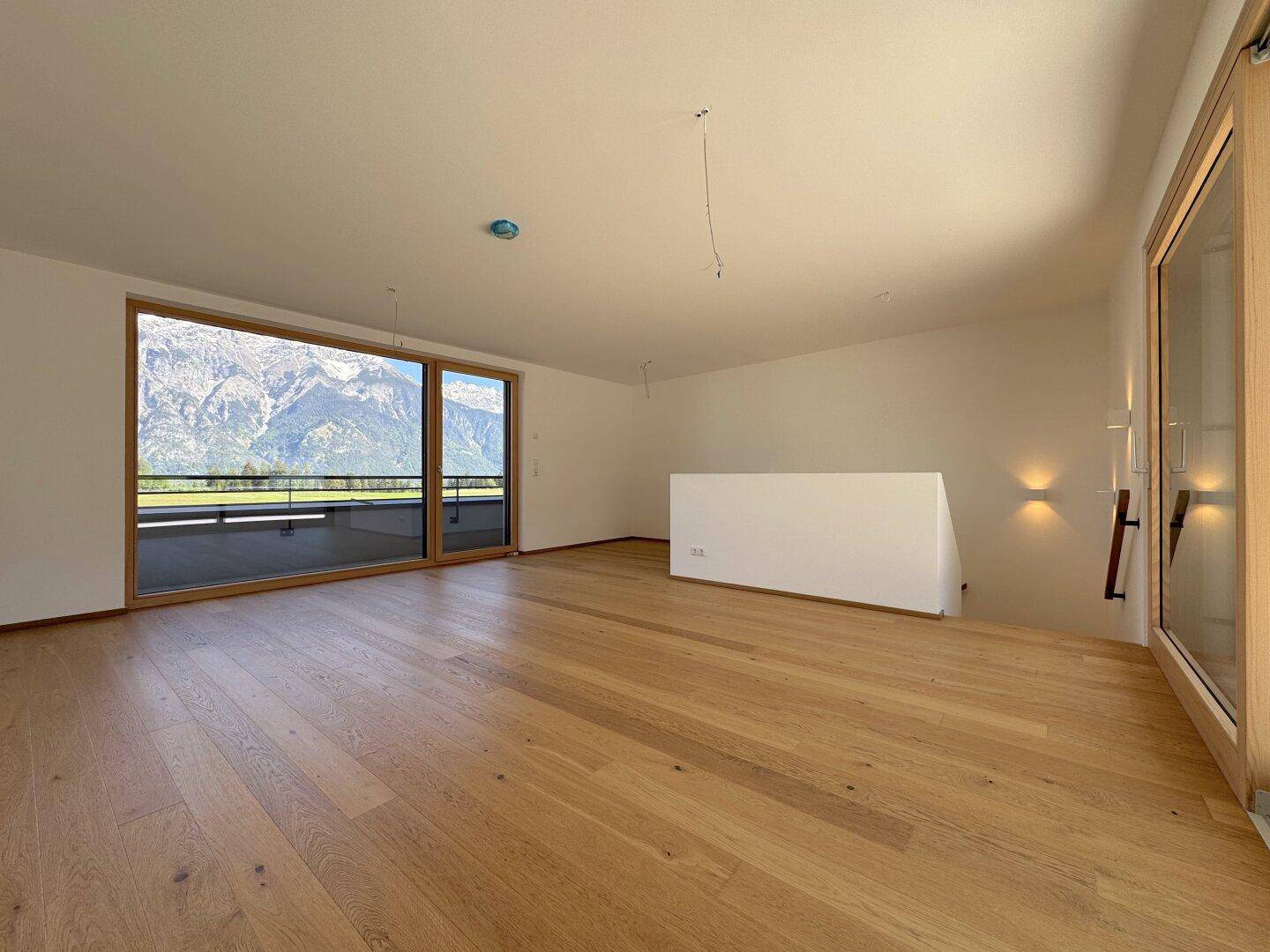 Geräumiger, unmöblierter Raum mit Holzboden und Panoramafenstern, die einen beeindruckenden Bergblick freigeben.