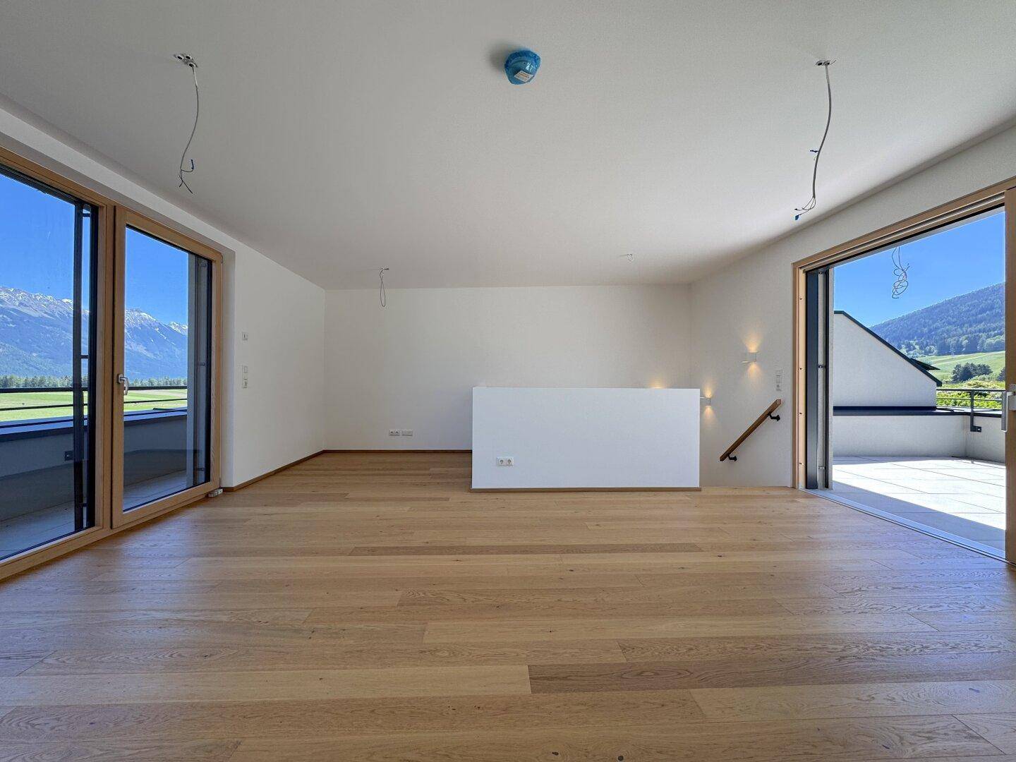 Heller, unmöblierter Raum mit Holzboden und großen Schiebetüren, die einen weiten Bergblick bieten.
