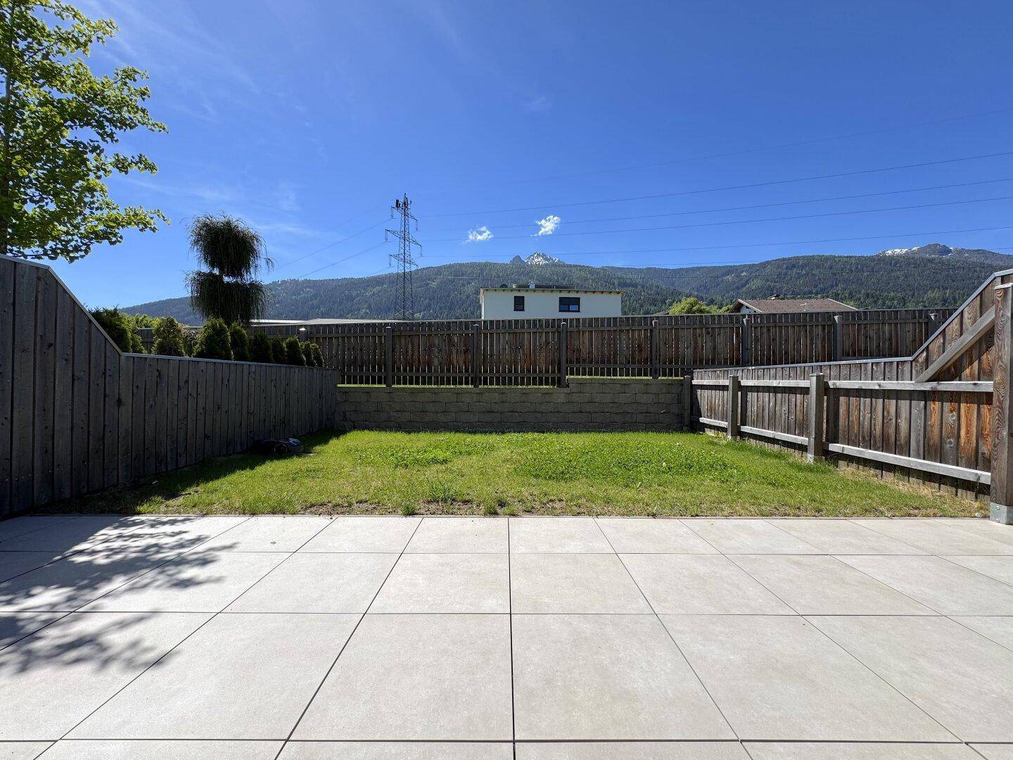 Kleiner, eingezäunter Gartenbereich mit Rasenfläche und einer gepflasterten Terrasse.