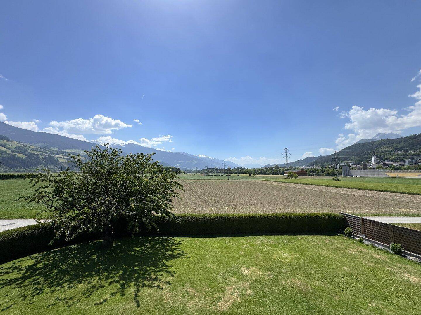 Weitläufiger Blick über grüne Felder und die umliegende Berglandschaft an einem sonnigen Tag.