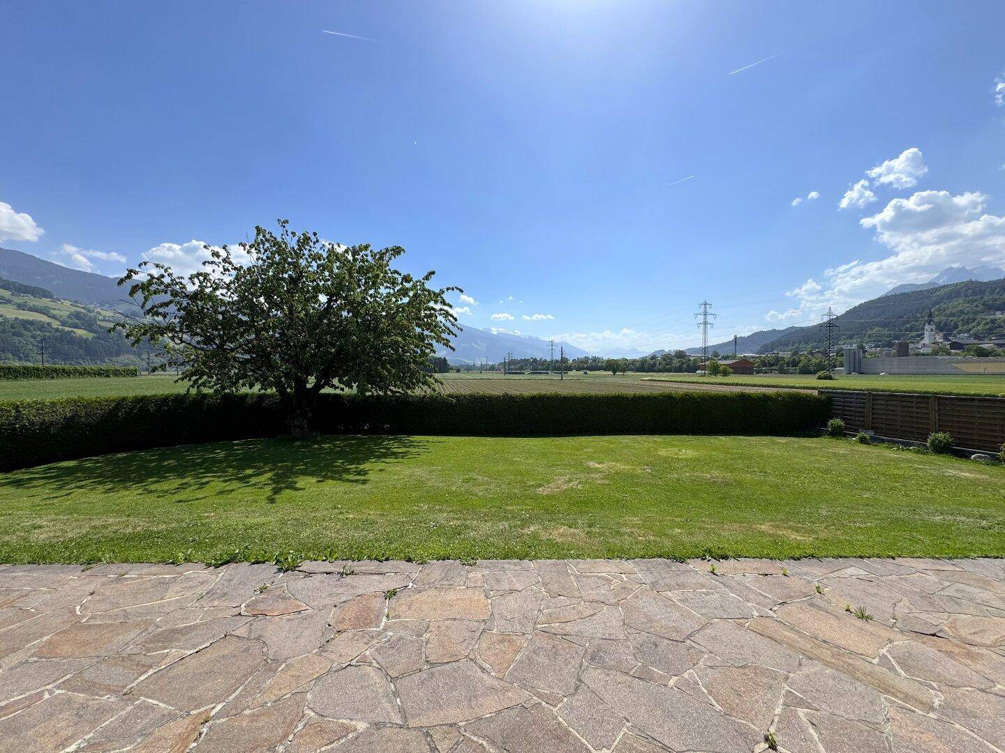 Weitläufiger Ausblick über den Rasen und die Felder bis zu den Bergen an einem sonnigen Tag.