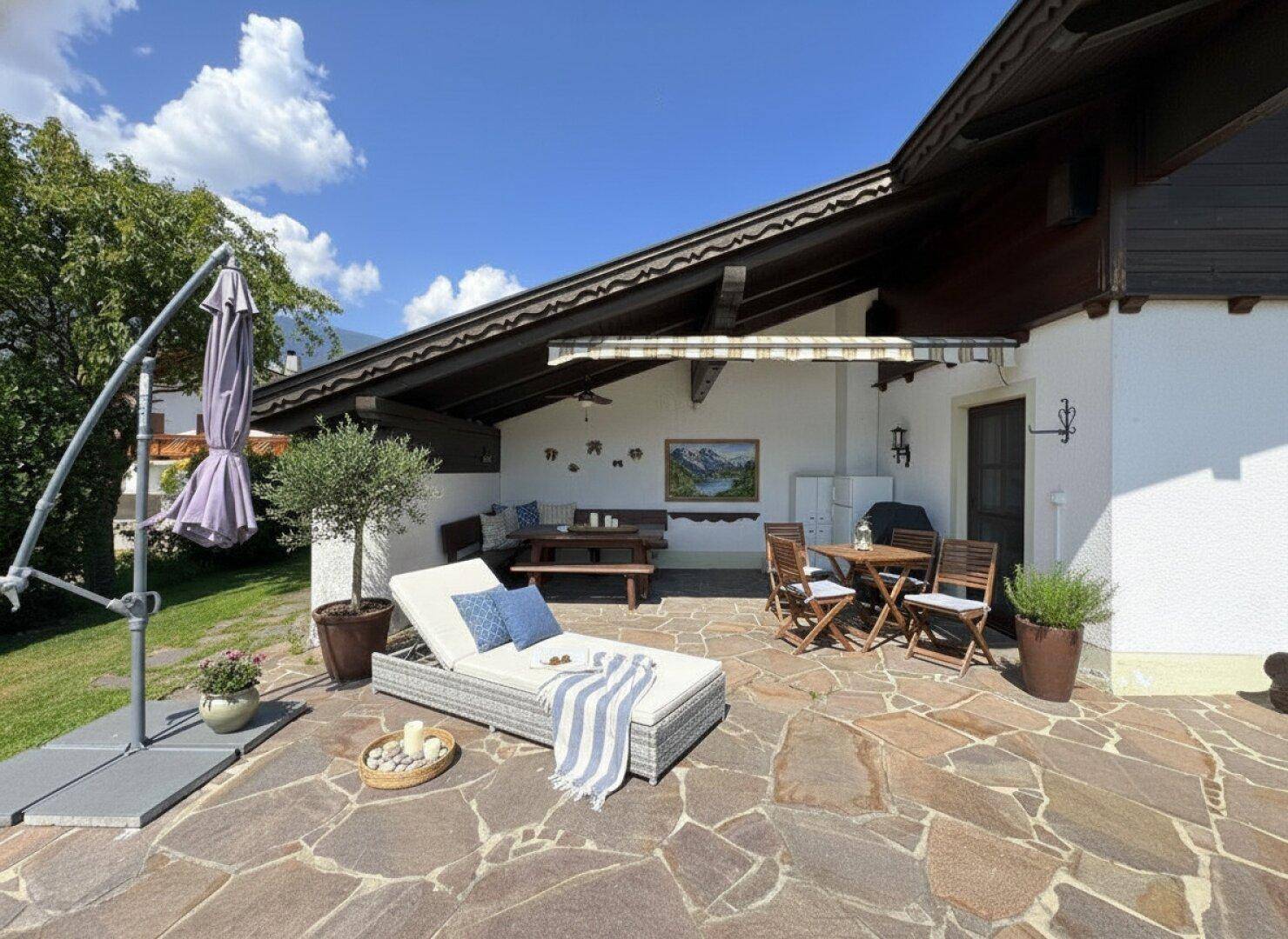 Gemütliche Steinterrasse mit Sonnenliege und Essbereich, ideal für entspannte Stunden im Freien.