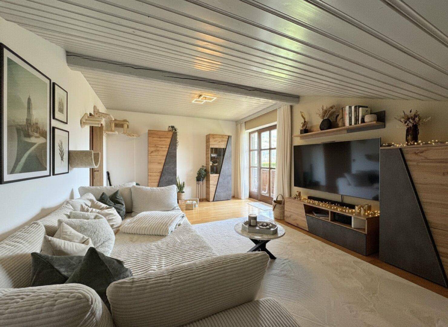 Modern eingerichtetes Wohnzimmer mit großem Sofa, TV-Möbeln und Zugang zum Balkon.