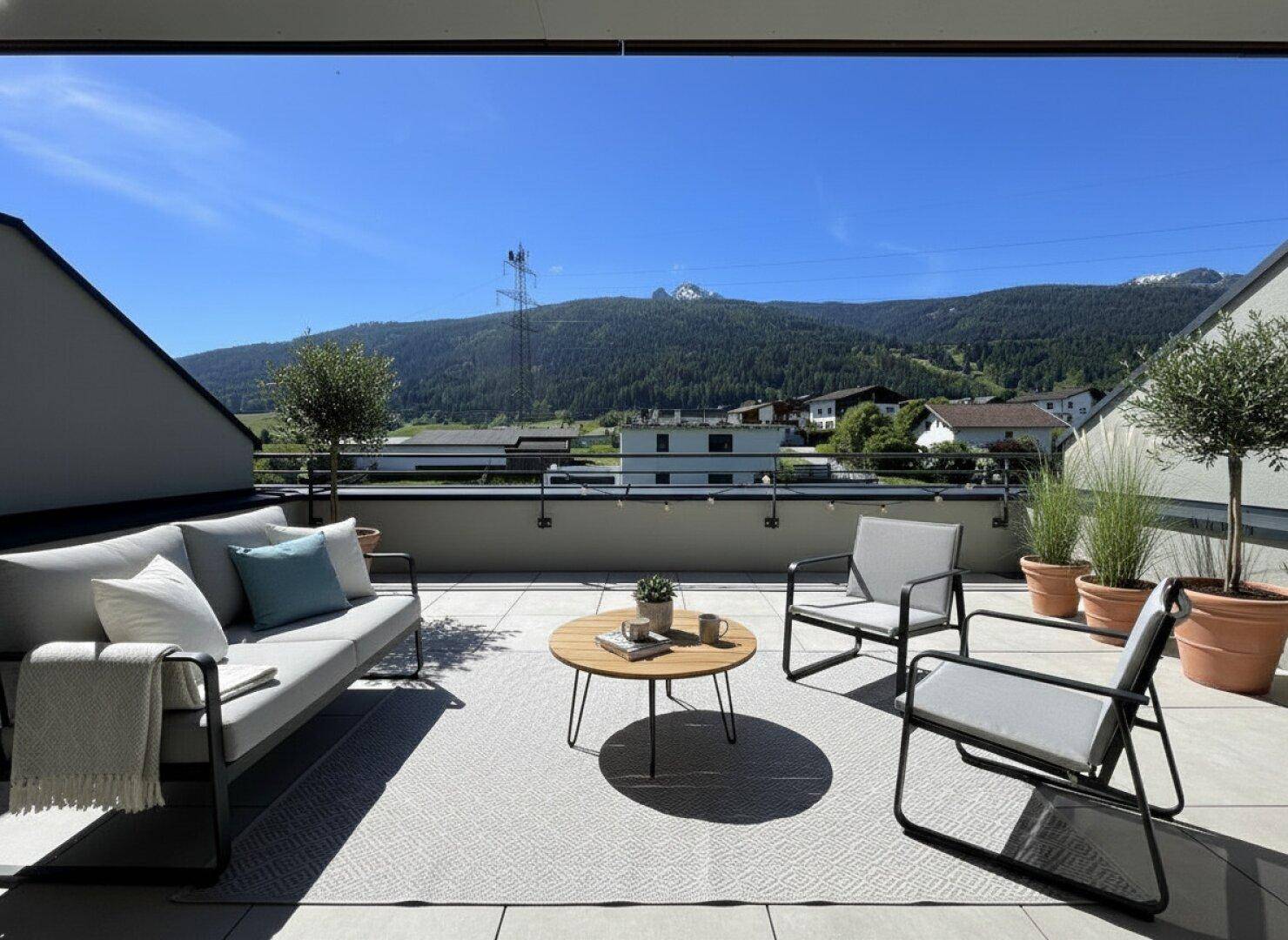 Sonnige Terrasse mit modernen Gartenmöbeln und einem weiten Blick auf die umliegende Berglandschaft.