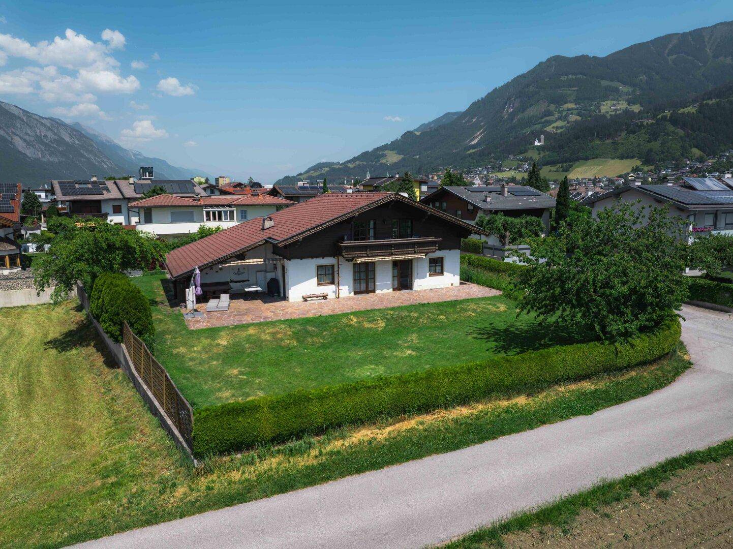 Luftaufnahme des Hauses mit gepflegtem Garten, umgeben von Wohnbebauung und Bergen.
