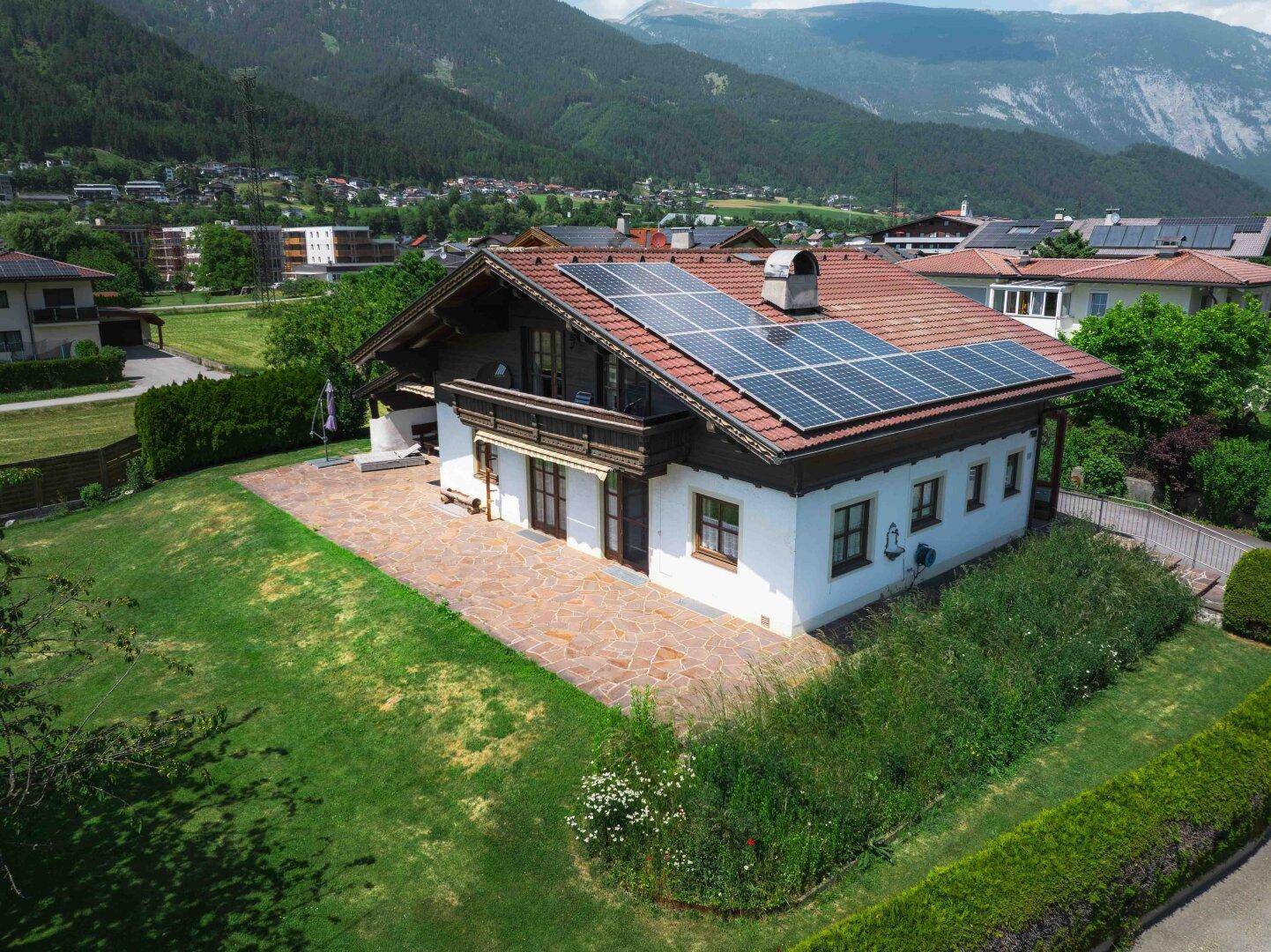 Dachansicht des Hauses mit Photovoltaikanlage und großer Steinterrasse, umgeben von Natur.