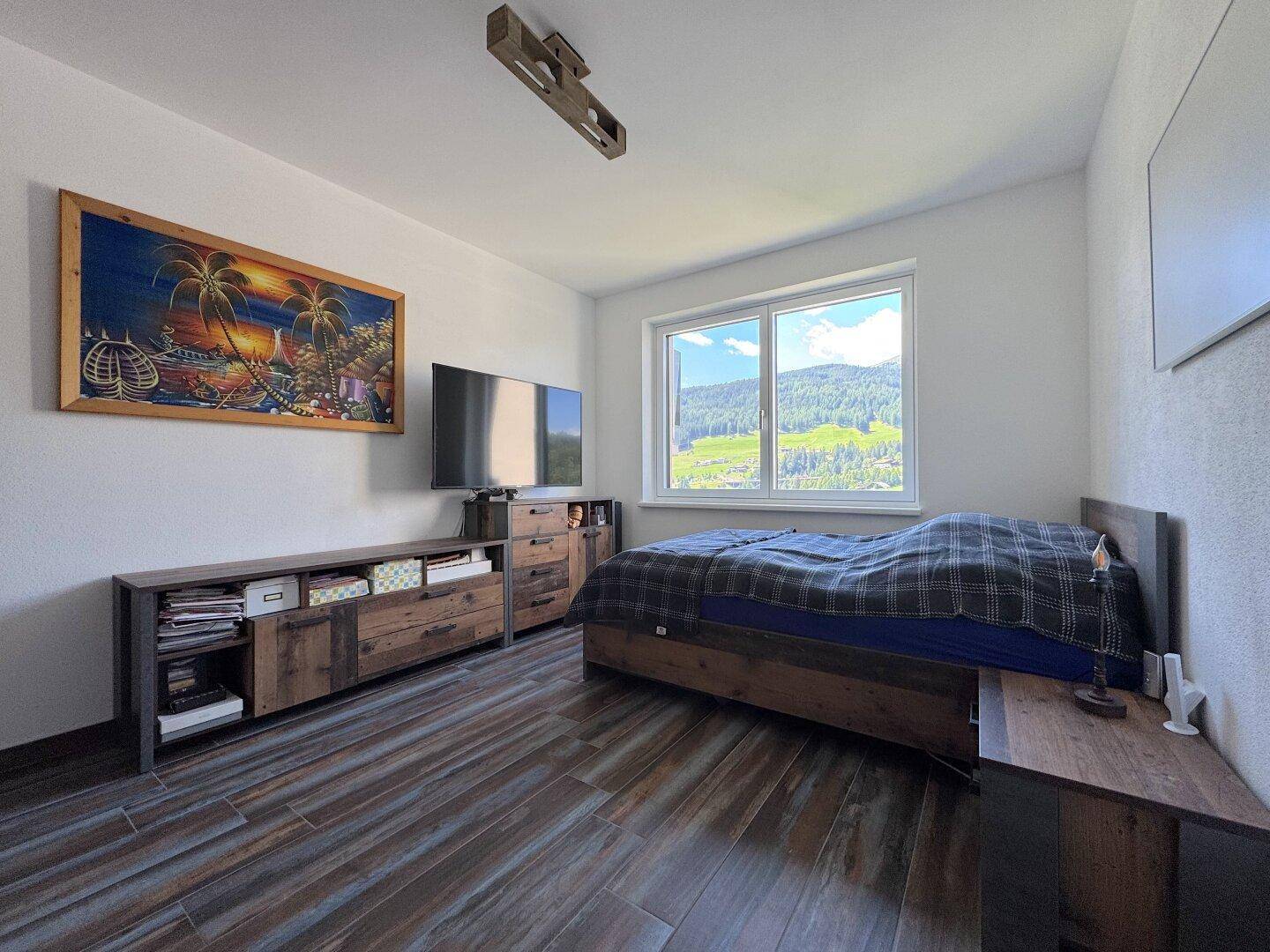 Gemütliches Schlafzimmer mit Holzboden, Fernseher und Fenster mit schöner Aussicht.