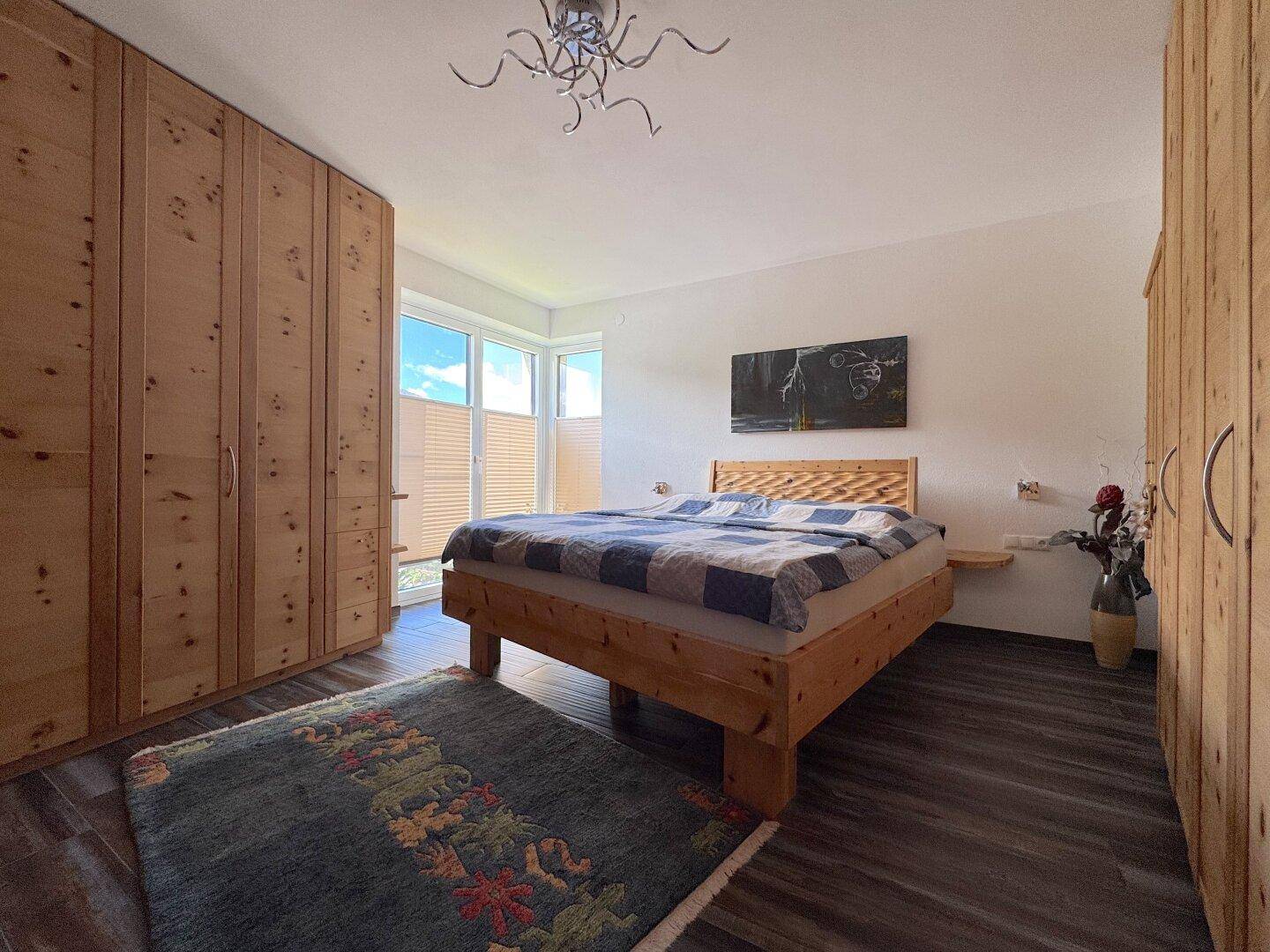 Helles Schlafzimmer mit Holzbett, Einbauschränken und Fenster mit Blick ins Grüne.
