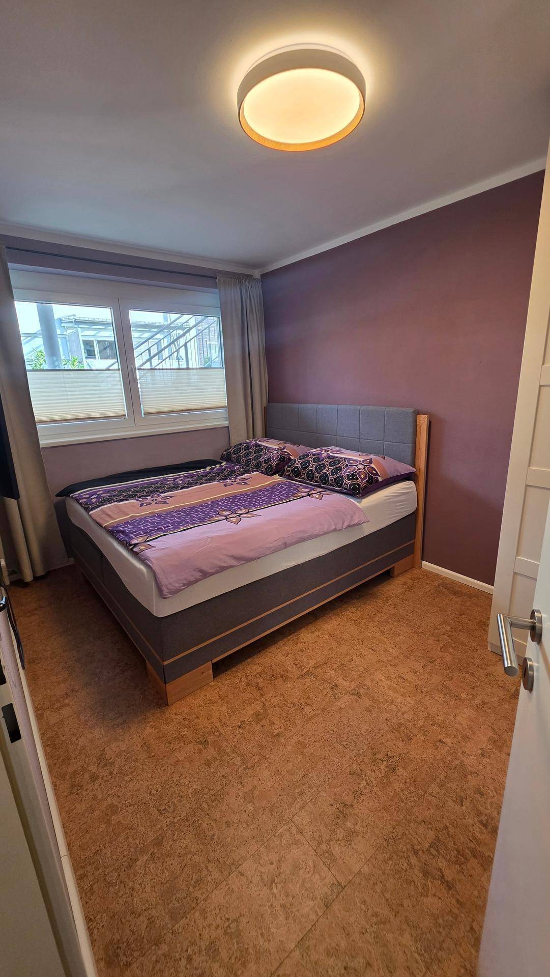 Gemütliches Schlafzimmer mit Doppelbett, Korkboden und einem Fenster.