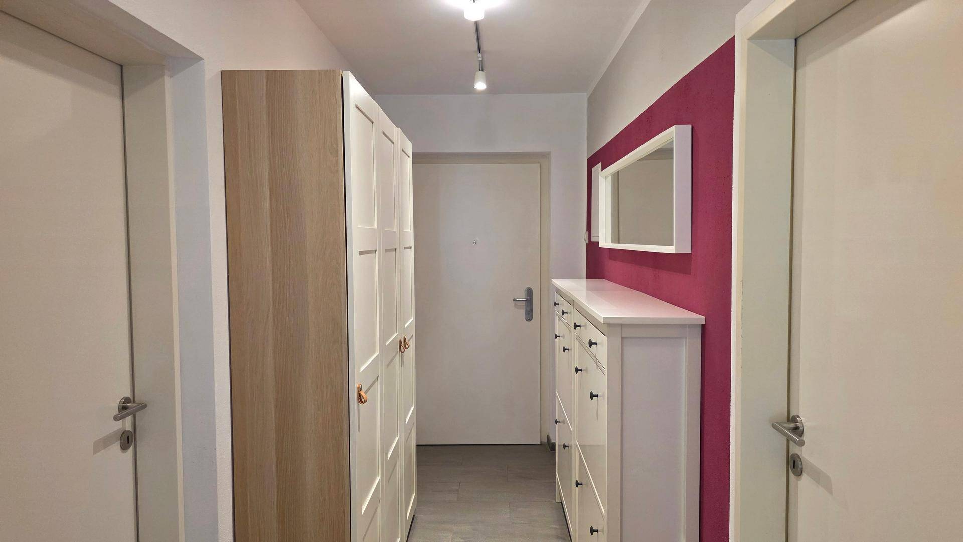 Heller Flur mit Garderobenschrank, Kommode und einem Spiegel an der Wand.