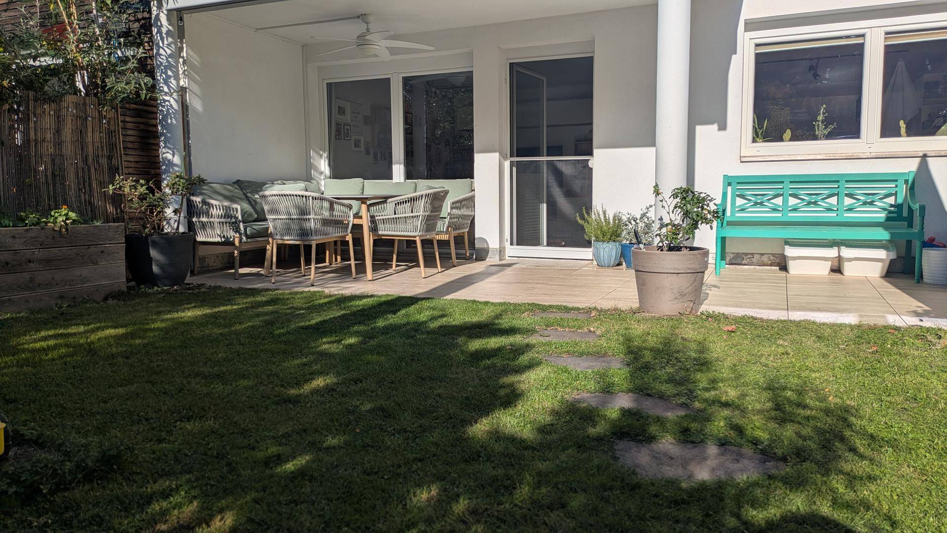 Sonniger Gartenbereich mit möblierter Terrasse und Rasenfläche vor dem Haus.