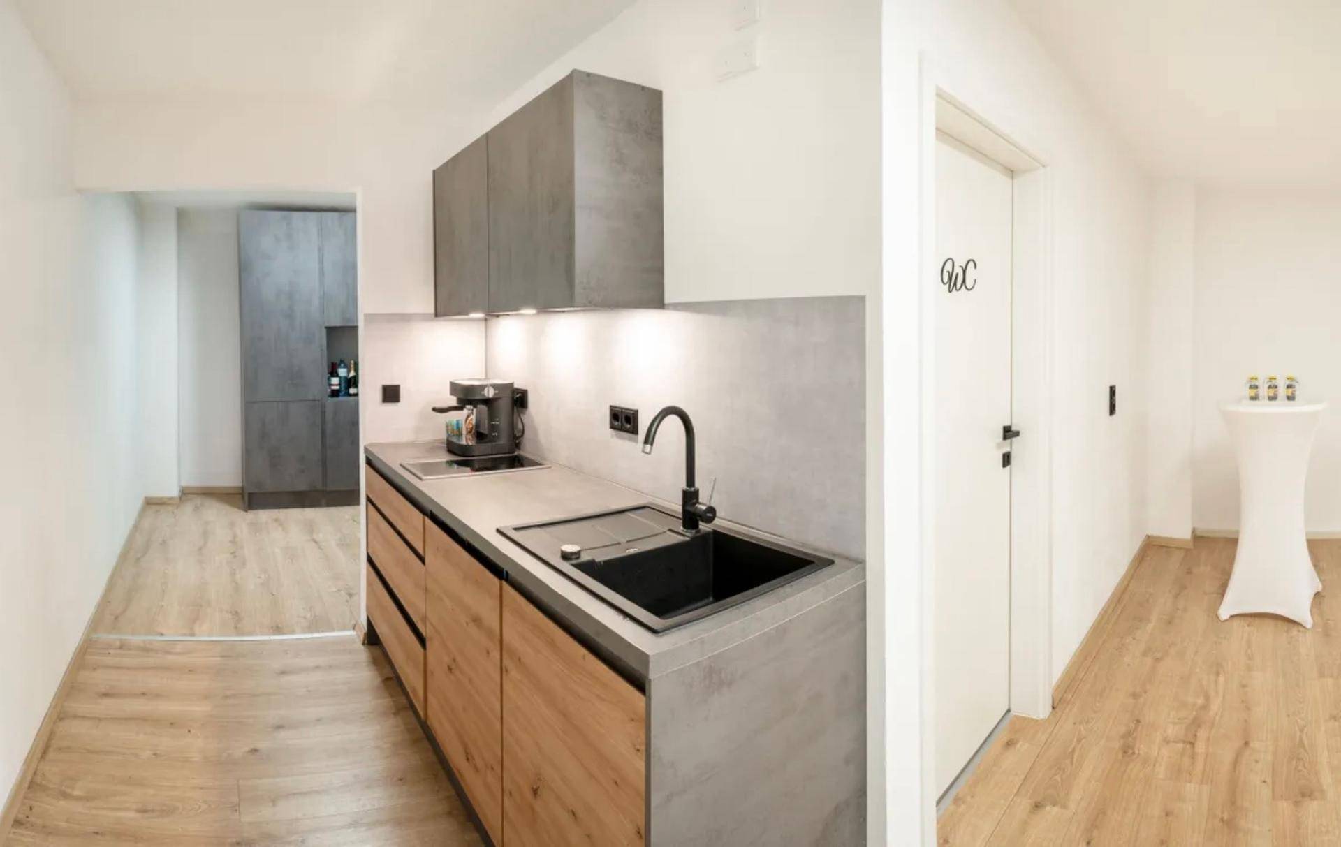 Funktionale Teeküche mit modernen grauen und holzfarbenen Schränken, Spüle und Kaffeemaschine.